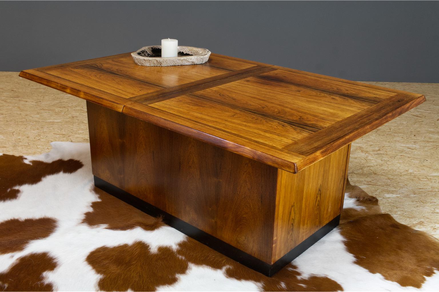Luxury Danish rosewood coffee table with dry bar in the style of Dyrlund. This beautiful made Scandinavian modern solid coffee table can be unfolded to reveal the hidden cabinet, and with use of the two black trays can be used in an elongated