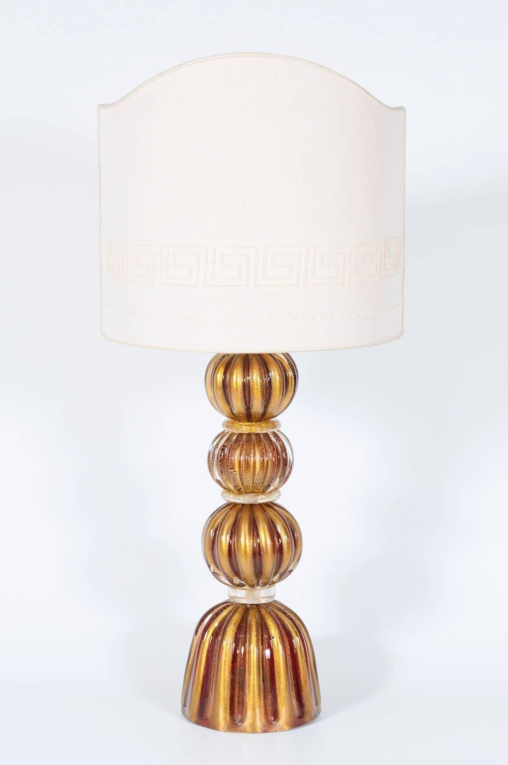 A Delicate Charming Murano Glass Table Lamp with Ruby Spheres and Gold Accents 1980s Italy.
This enchanting table lamp, crafted entirely by hand from Murano glass, exudes elegance and timelessness. The lamp's design features three gently ribbed
