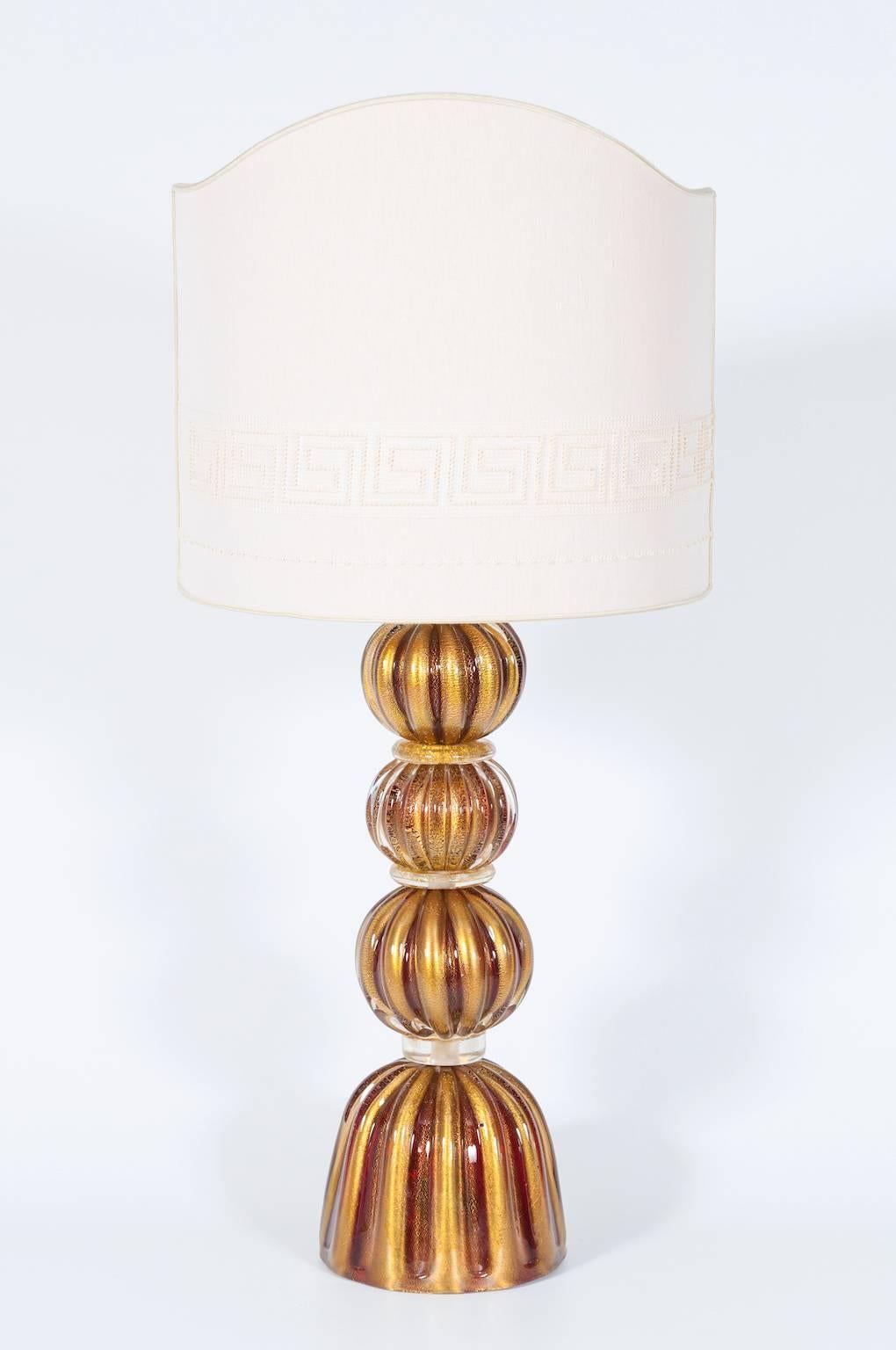 Delicata e affascinante lampada da tavolo in vetro di Murano con sfere di rubino e accenti dorati del 1980.
Questa incantevole lampada da tavolo, realizzata interamente a mano in vetro di Murano, emana eleganza e atemporalità. Il design della
