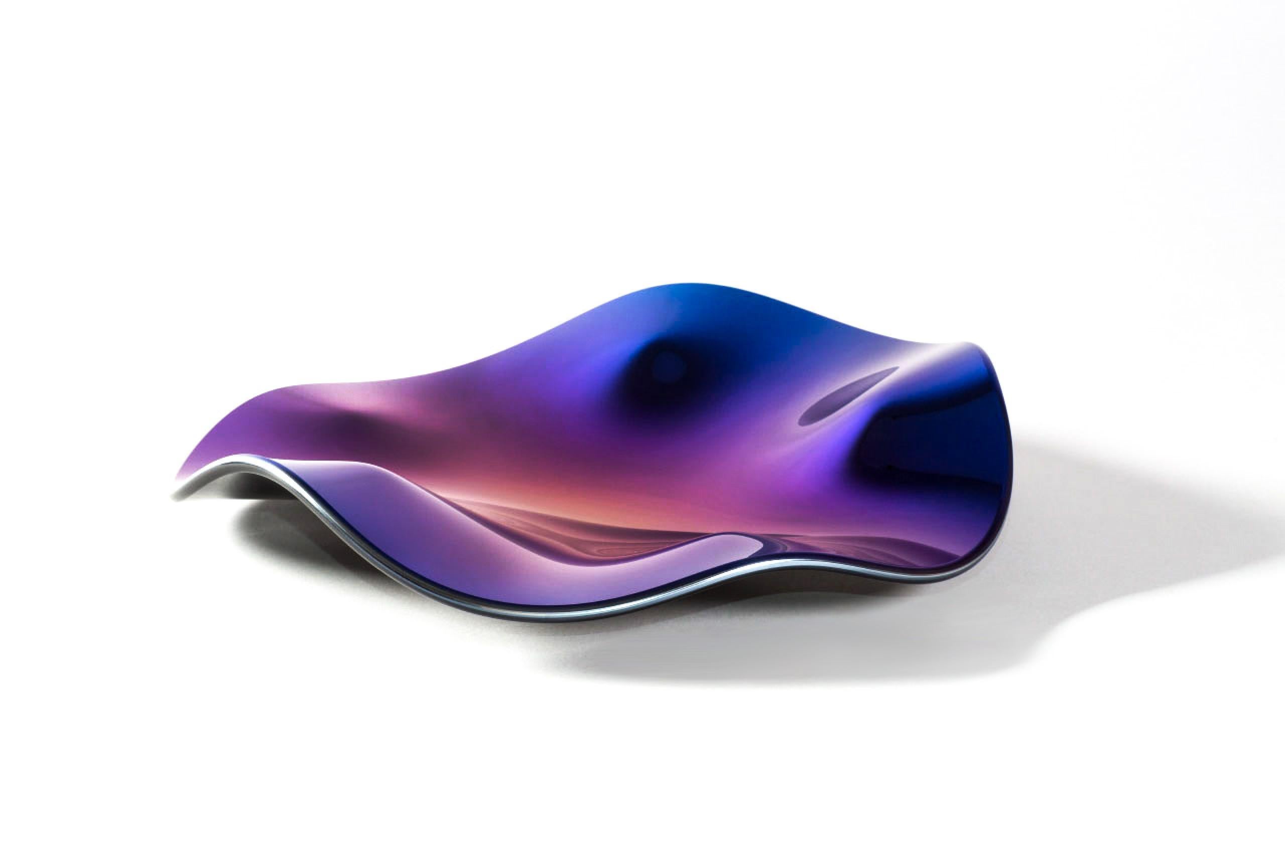 Des colloïdes de manganèse et de rubis colorent le corps ; une brume de titane prune oscille entre le violet royal et la cerise noire sous une lumière changeante. Le bord asymétrique adoucit les géométries strictes, faisant de ce plat décoratif un