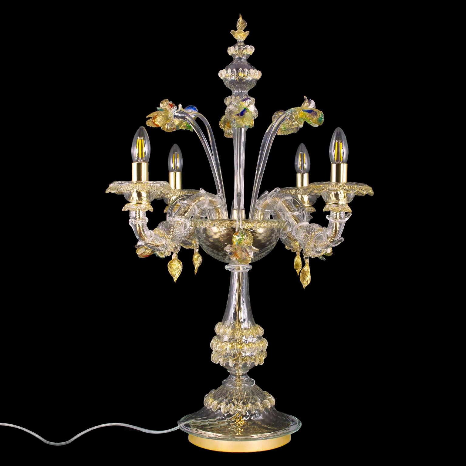 Lussuosa lampada Rezzonico flambeau a 4 bracci, in vetro di Murano trasparente e dorato di Multiforme.
La lampada flambeau è una lampada da tavolo davvero elegante e lussuosa, arricchita da fiori. Le luci sono verso l'alto. 
Adatto a illuminare ogni