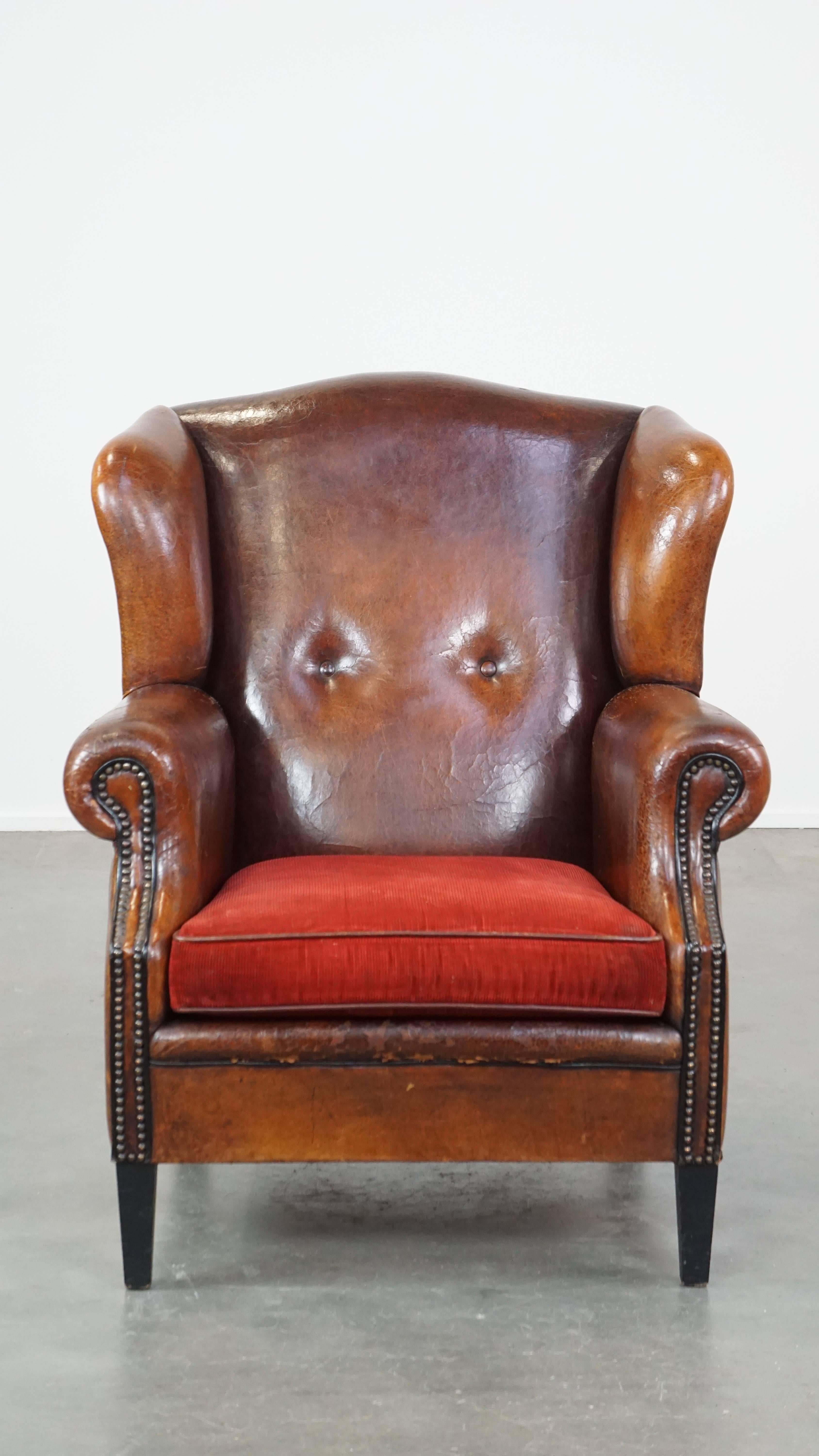 Este sillón de piel de oveja, con sus colores profundos, el cojín del asiento de pana roja y el ribete con cabeza de clavo, tiene un carácter lujoso y refinado. El sillón está muy bien acabado y ha desarrollado una pátina impresionante. Tiene un
