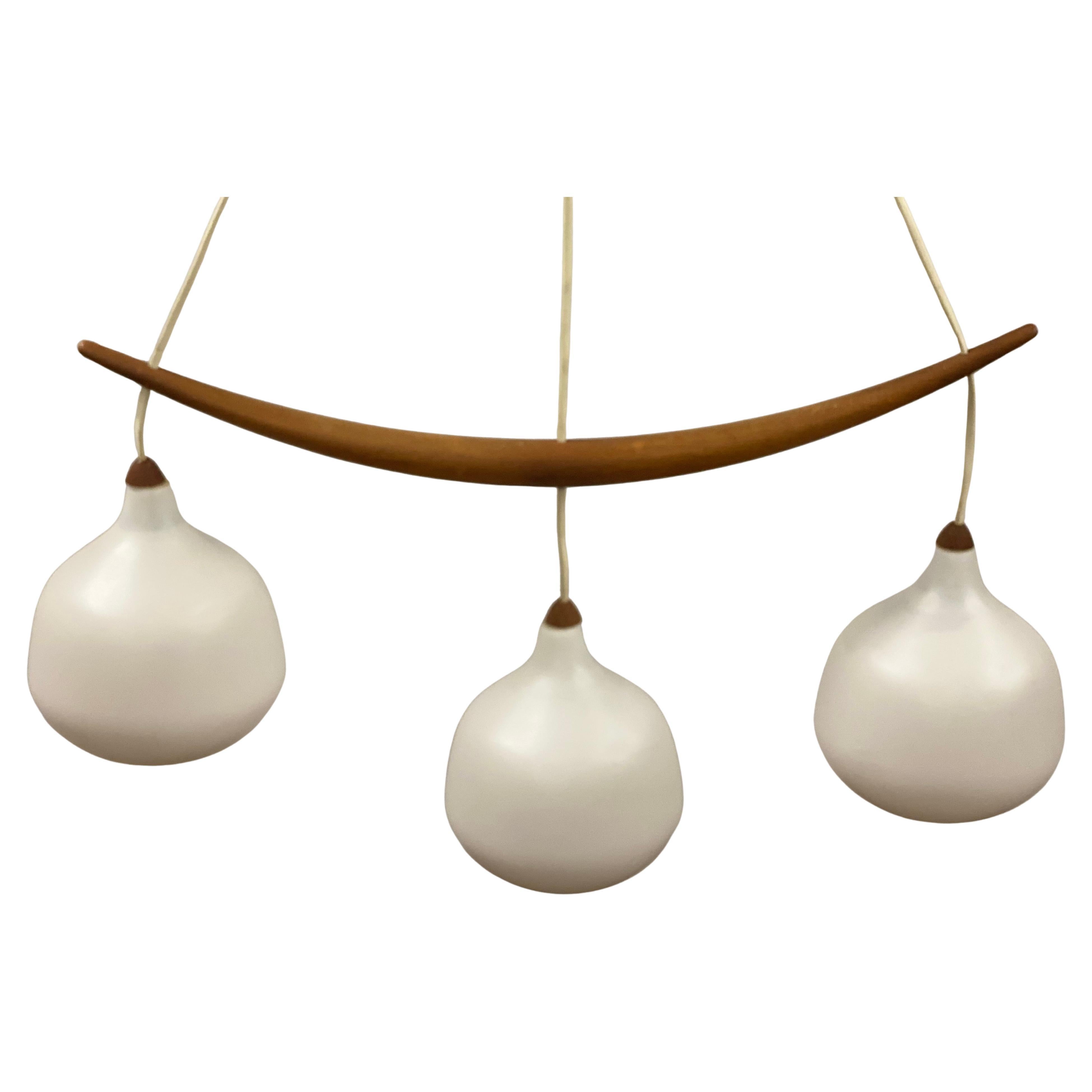 Pendente Bananen svedese Luxus Model 521 in teak e vetro bianco a tre luci. Disegnato da Uno/One Kristiansson. Un'elegante lampada caratterizzata da un gancio curvo in teak massiccio con tre paralumi a bulbo in vetro smerigliato bianco, ciascuno dei