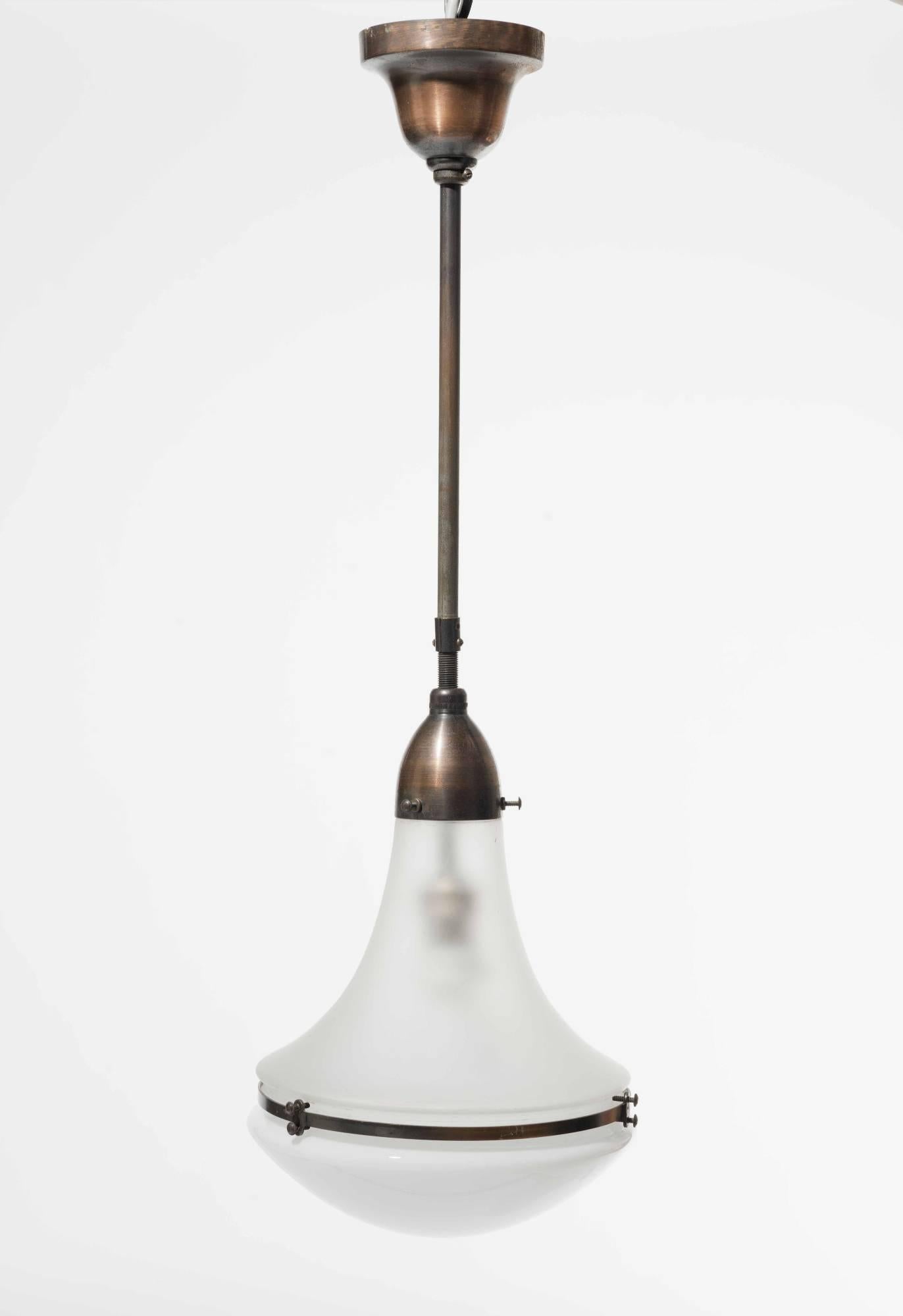 This classic Peter Behrens design piece from circa 1910 was manufactured in Germany by SSW (Siemens-Schuckert-Werke GmbH). A frosted white glass shade is held in place by a bell-shaped metallic attachment and stem, encasing the bulb for the