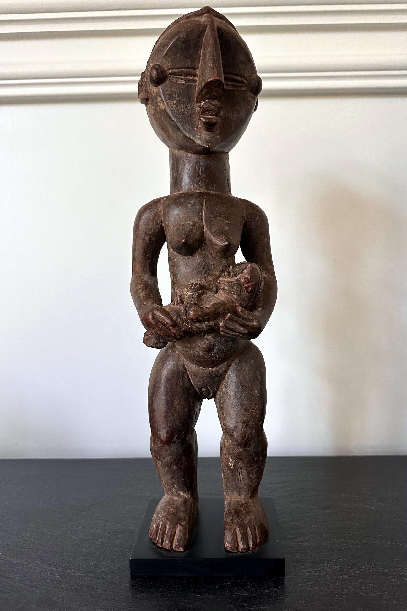 A finely carved Lwalwa maternity figure holding a baby from Democratic Republic of Congo in Central Africa circa 20th century. The statue was acquired in 2006 from the collection of Jean-Pierre Hallet Collection of African Art. 
The figure, with her