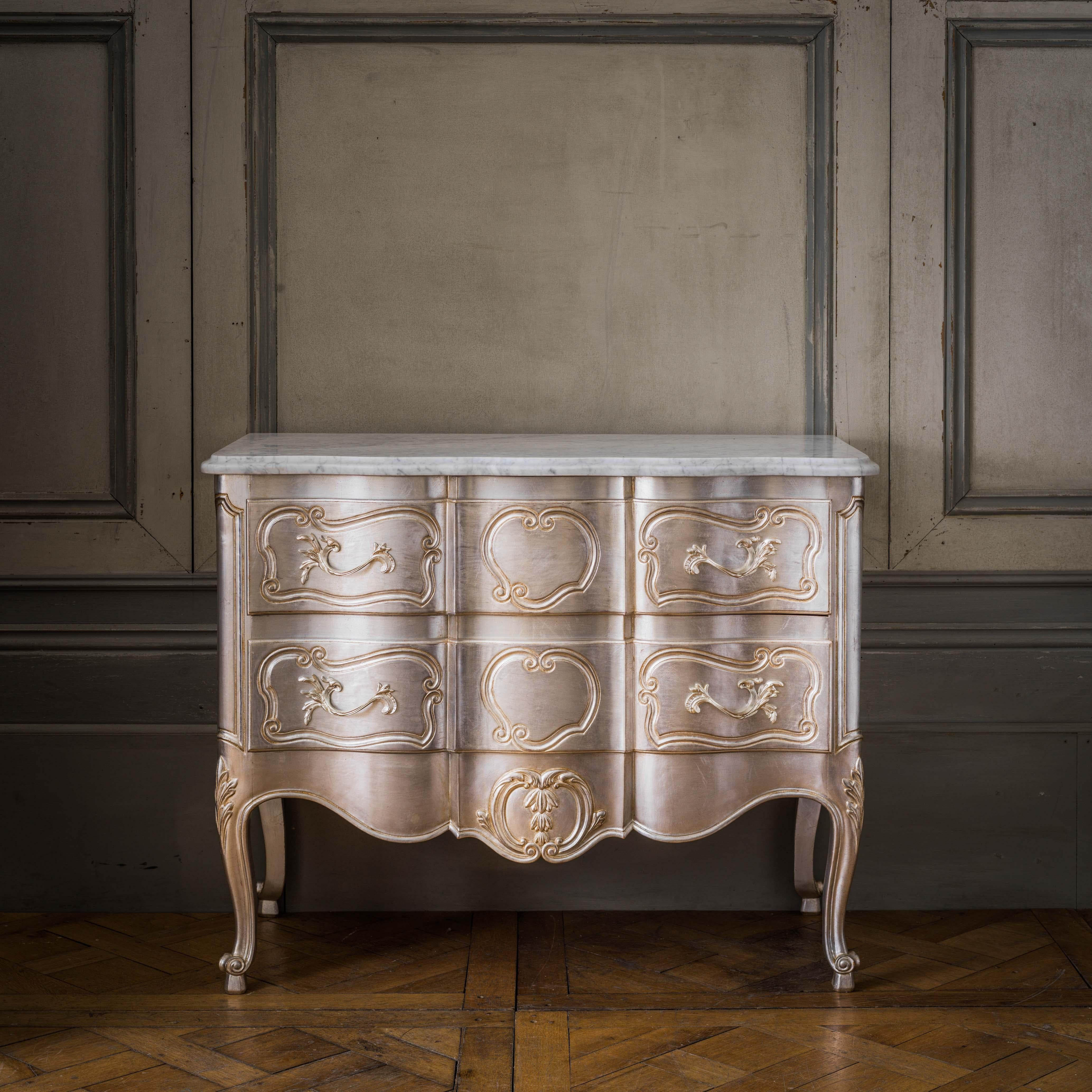 A LXV style chest of drawers, hand carved to order and custom finished. The picture shows the piece in a hand gilded silver finish with a beveled white Carrara marble top.