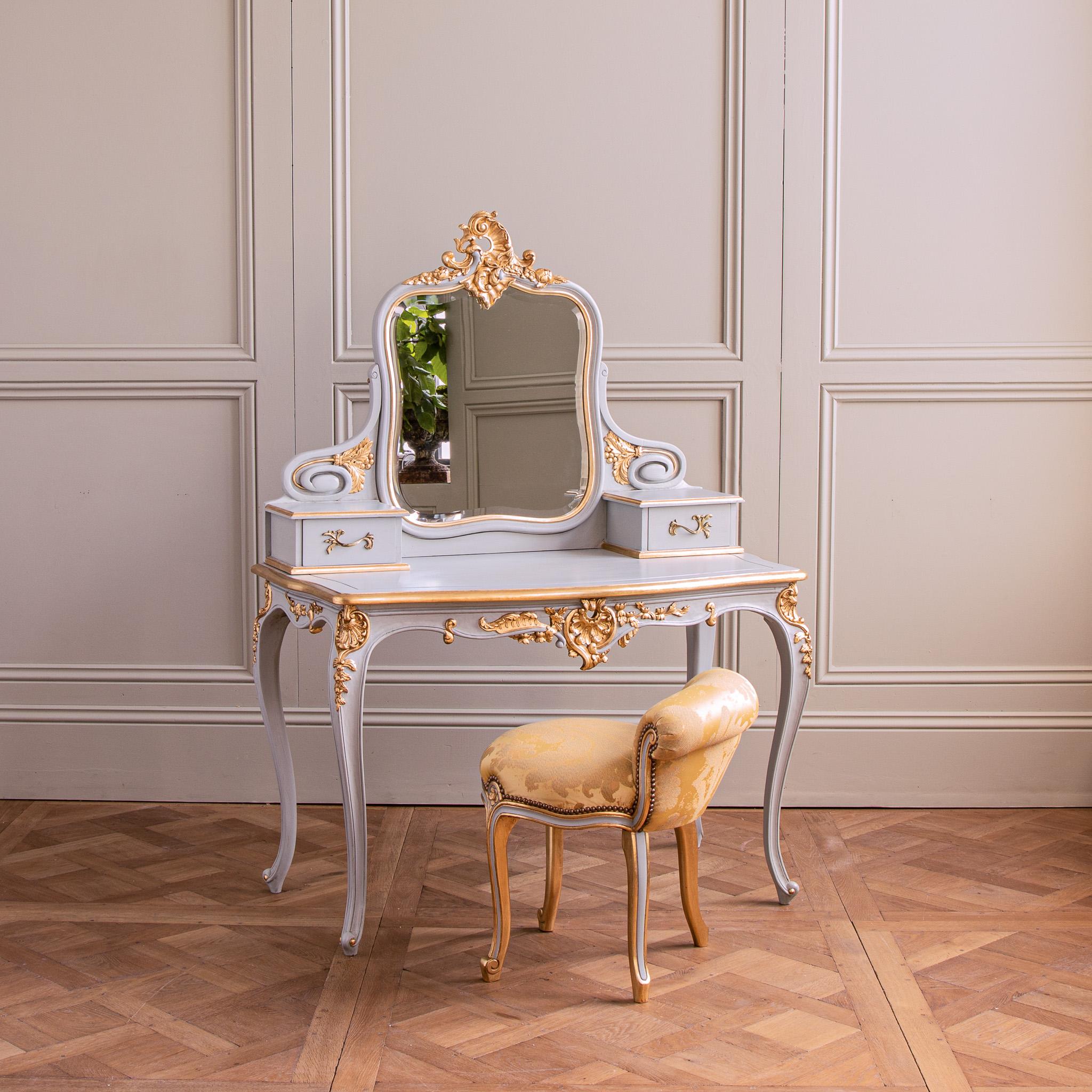 Made in the French LXV style, this dressing table has been hand carved in solid wood, featuring the ornamental shell of the Rococo period. The design integrates a large adjustable mirror with two side drawers featuring aged bronze handles which have