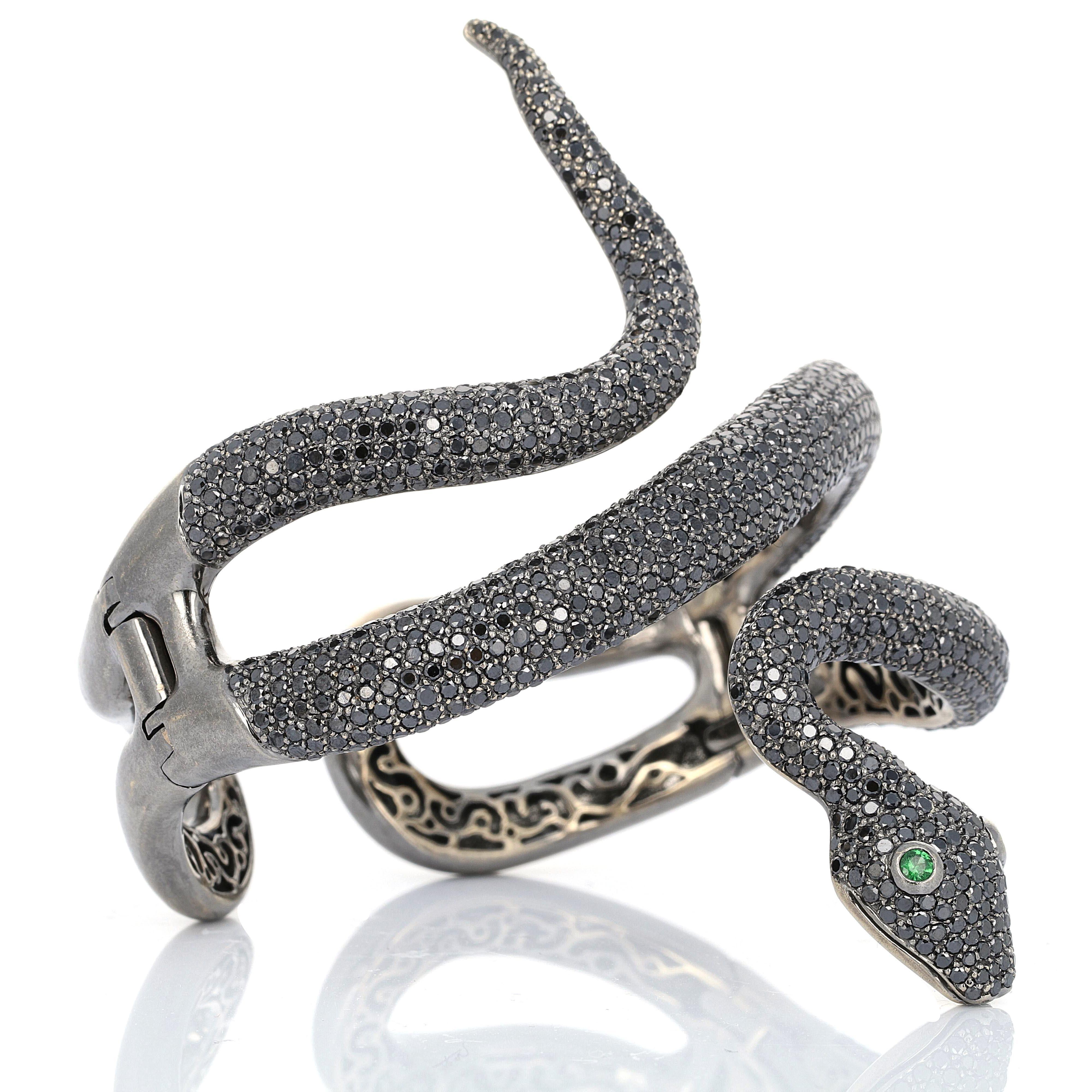 This Lydia Courteille diamond and garnet black rhodium 18 karat white gold snake bangle is intricately set with 14.33 carats of black diamonds. The bangle coils tightly around the wrist creating an avante guard eccentric look. The eyes are made with