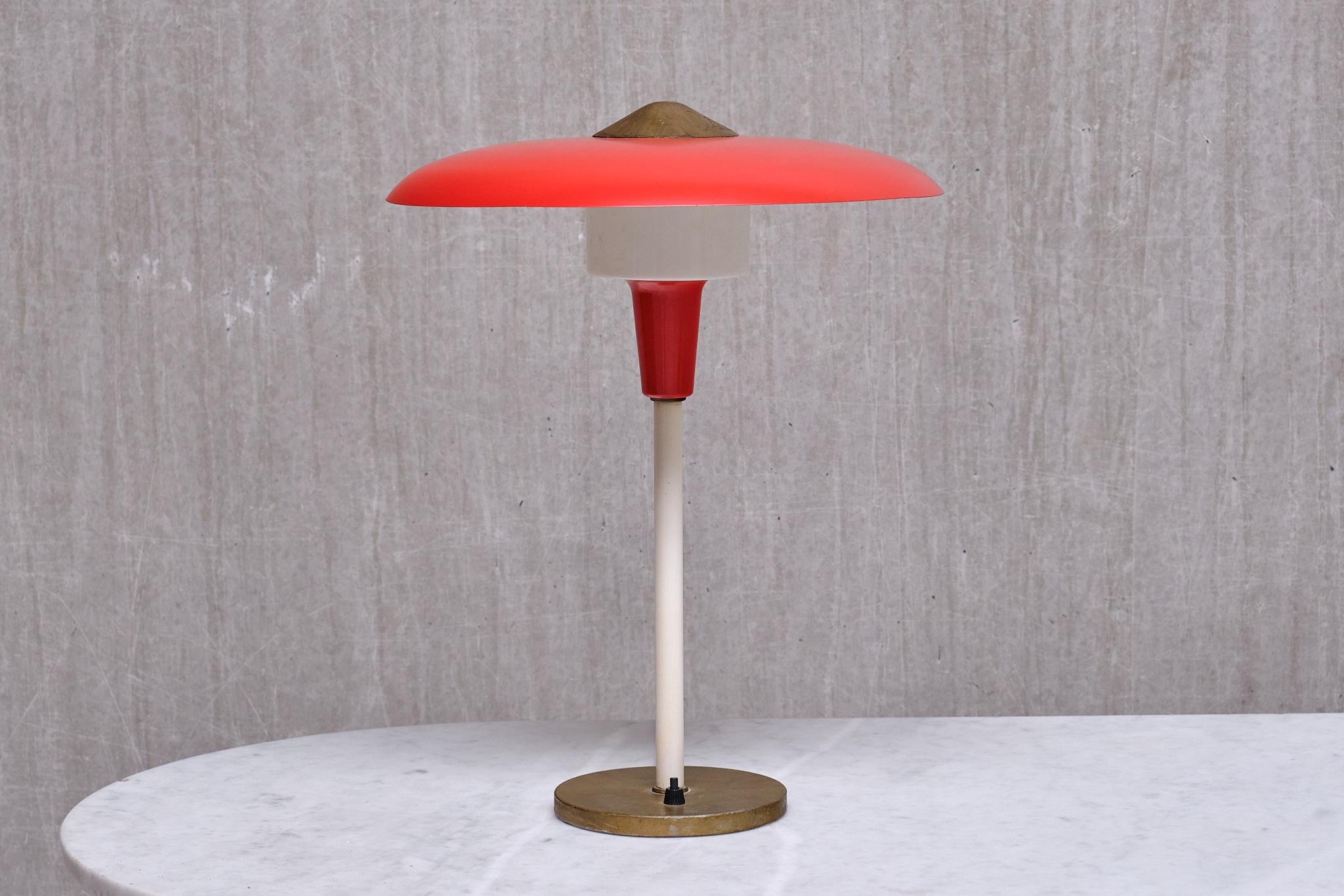 Cette rare lampe de table/de bureau a été produite par Lyfa au Danemark à la fin des années 1950.

Le design frappant est marqué par l'abat-jour en métal laqué rouge et la partie porteuse de la douille dans la même nuance de rouge. La tige centrale