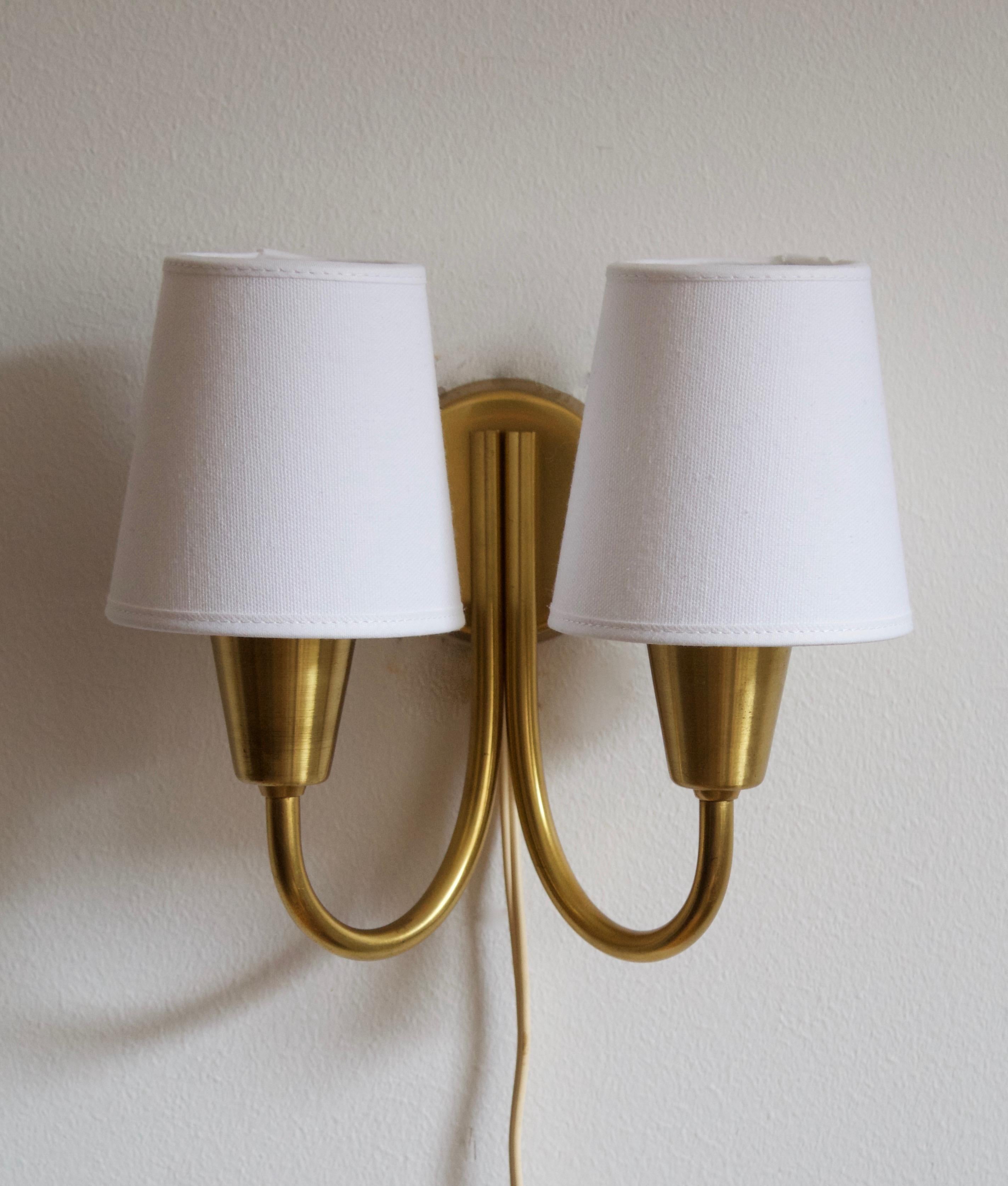 A two-armed wall sconce / wall light, designed and produced by Lyfa, Denmark, 1950s. Originally mounted with glass shades, now with brand new linen lampshades. 

Other designers of the period include Paavo Tynell, Jean Royère, Josef Frank, Kaare
