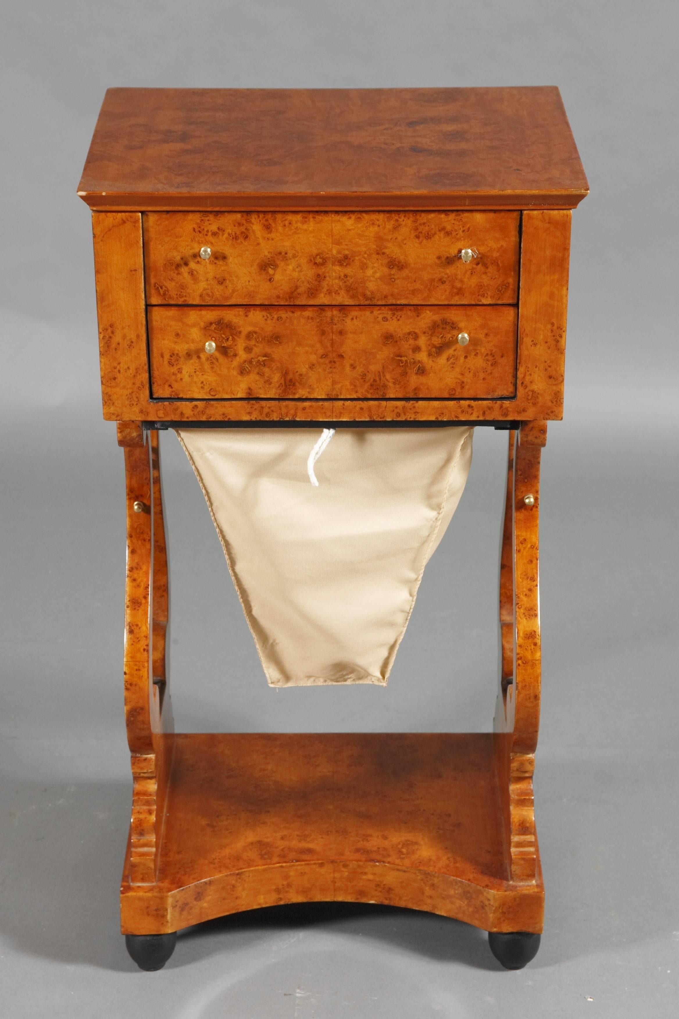 Bird's-eye on solid conid beechwood. Straight, bipedal base on lyre-shaped, perforated cheeks with metal sides. Underneath pull-out woolen drawer. Four-sided base plate. Top drawer with compartment. Overlapping, rectangular, fold-up plate.
 