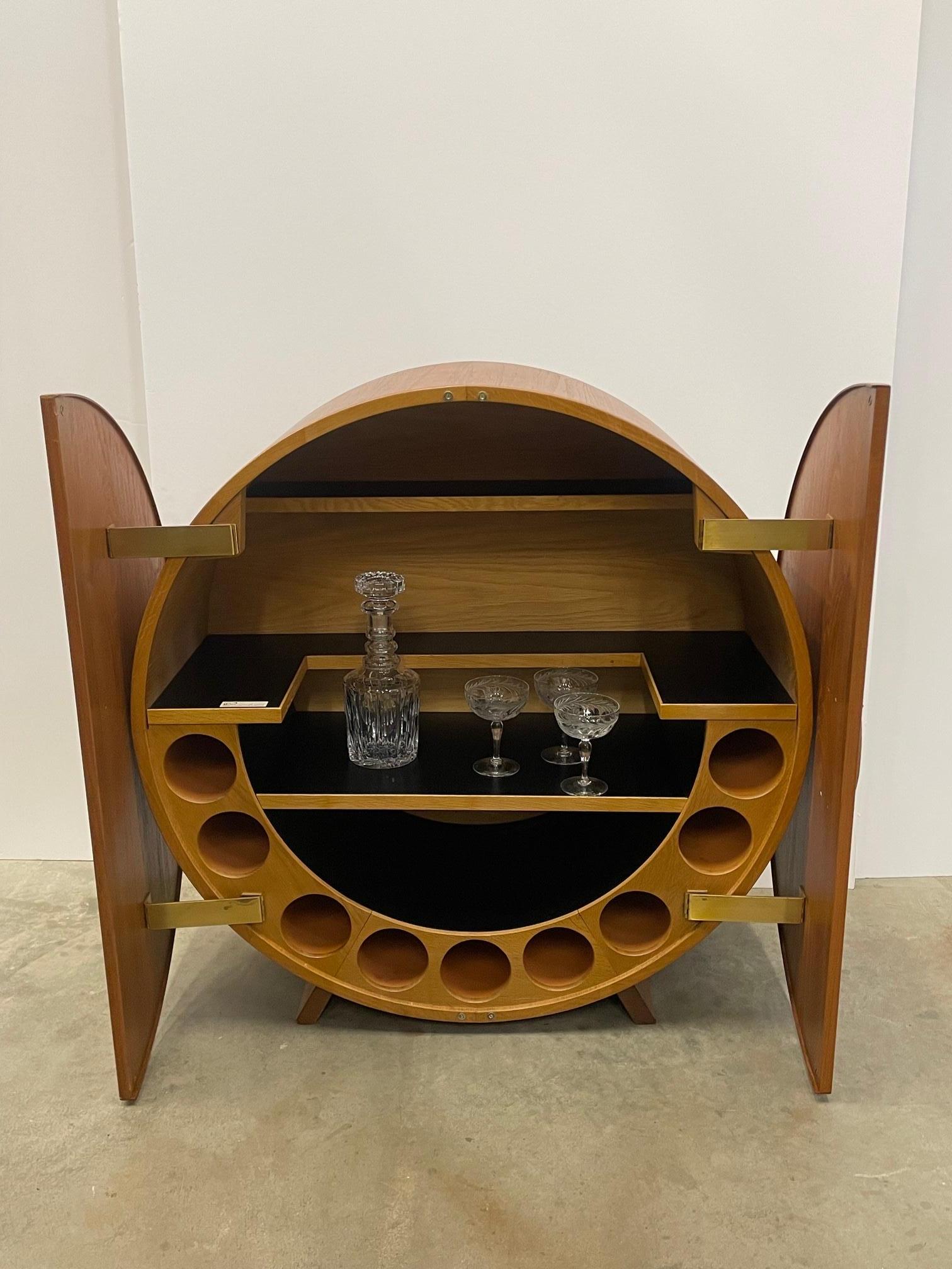 Ingenious teak Danish Mid-Century Modern disc shaped round dry bar having doors that pivot to the sides of the cabinet and reveal a fabulously outfitted interior bar with laminate shelves and places for bottles or glasses. There are brass hinges and
