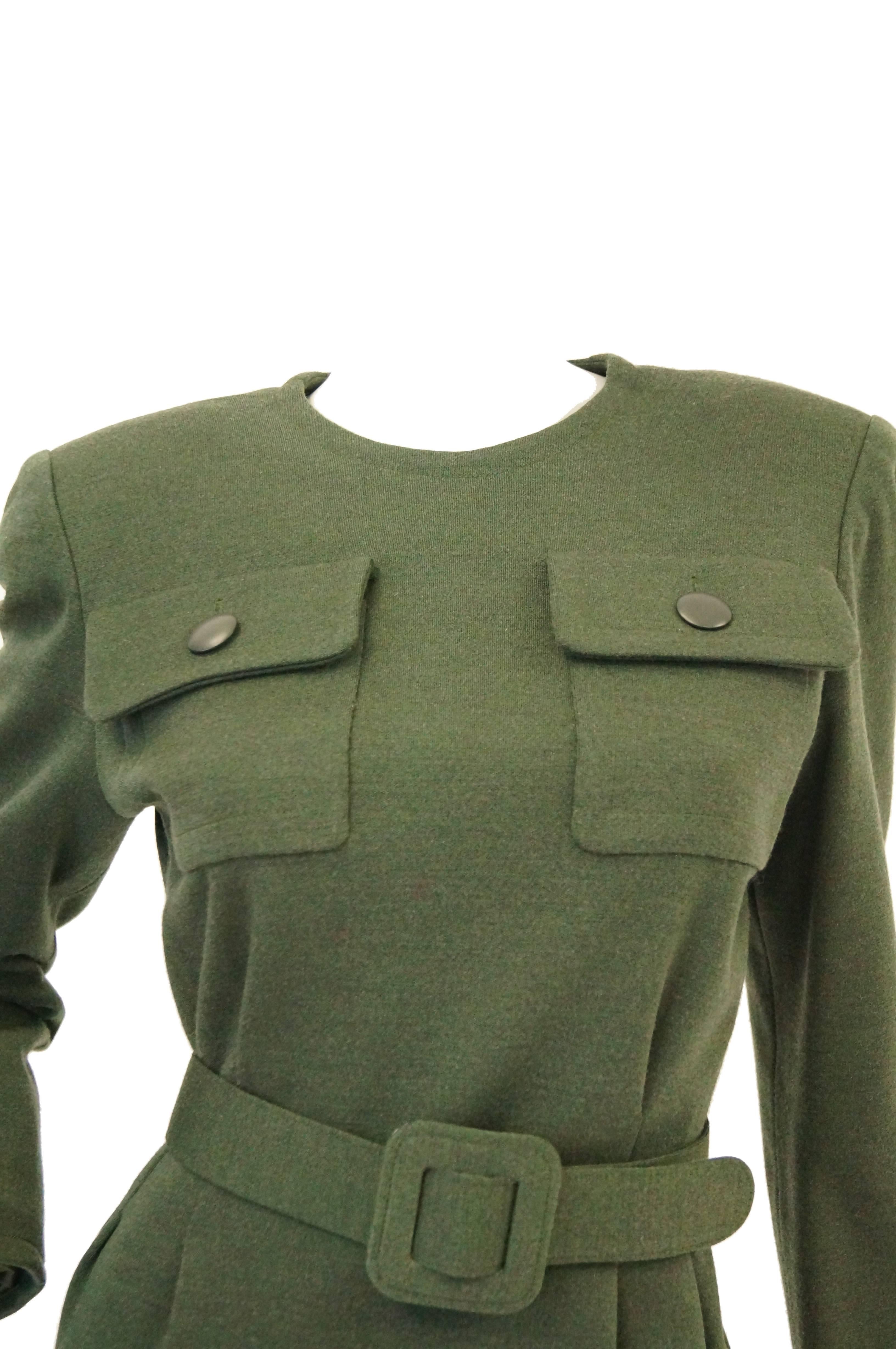 Understated and versatile olive green wool dress by Hubert de Givenchy. The dress hits at the knees, is long sleeved, and has a tight jewel neckline. The dress features two button closure flap pockets at the bust, a wide waist - cinching belt with
