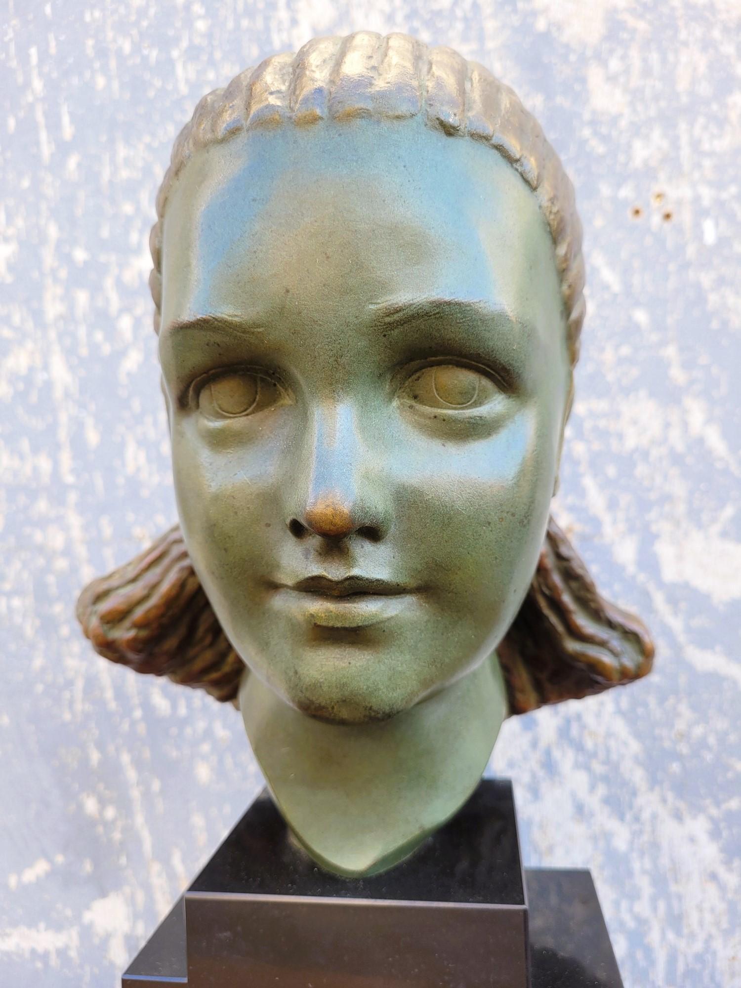 Bronze head of a woman with a green patina and light golden highlights, on a stepped base in black marble.

She wears an atypical hairstyle, with a small lock that comes back along the ear

This sculpture is signed Bouraine (Marcel,
