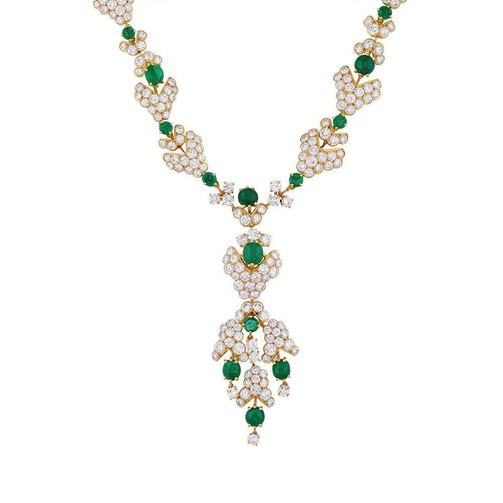 A gold, diamond and emerald demi-parure by M. Gerard, French, of foliate and blossom motif, consisting of a pair of ear pendants and a necklace of articulated links set with round brilliant-cut diamonds and interspersed with emeralds of alternating