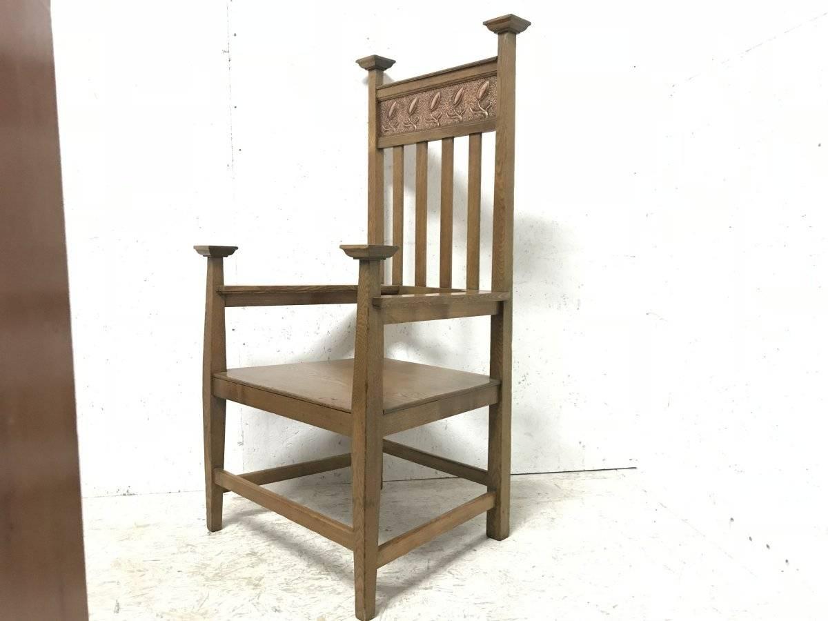 An Arts & Crafts ash wood armchair with square caps and an embossed copper panel with a row of tulips in the style of Baillie Scott to the top. The arms are quite unusual and wrap around internally to the back making a somewhat stronger yet subtle