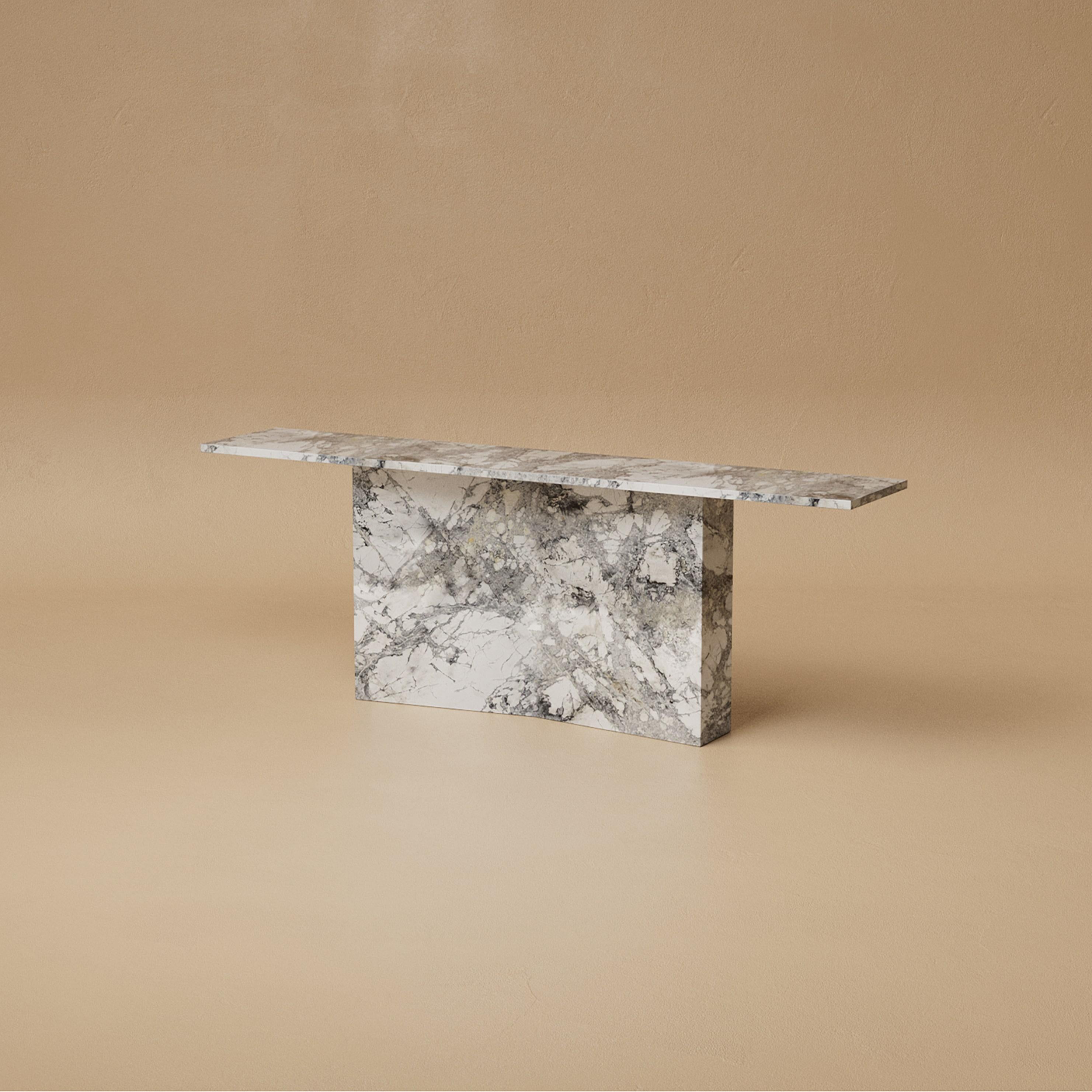 La Consola Marmont es atrevida en su silueta y refinada en sus detalles. Una base en forma de pajarita, revestida de piedra, sostiene una superficie monolítica que se siente a la vez imponente y elevada. Su geometría es pura y deliberada, creando un