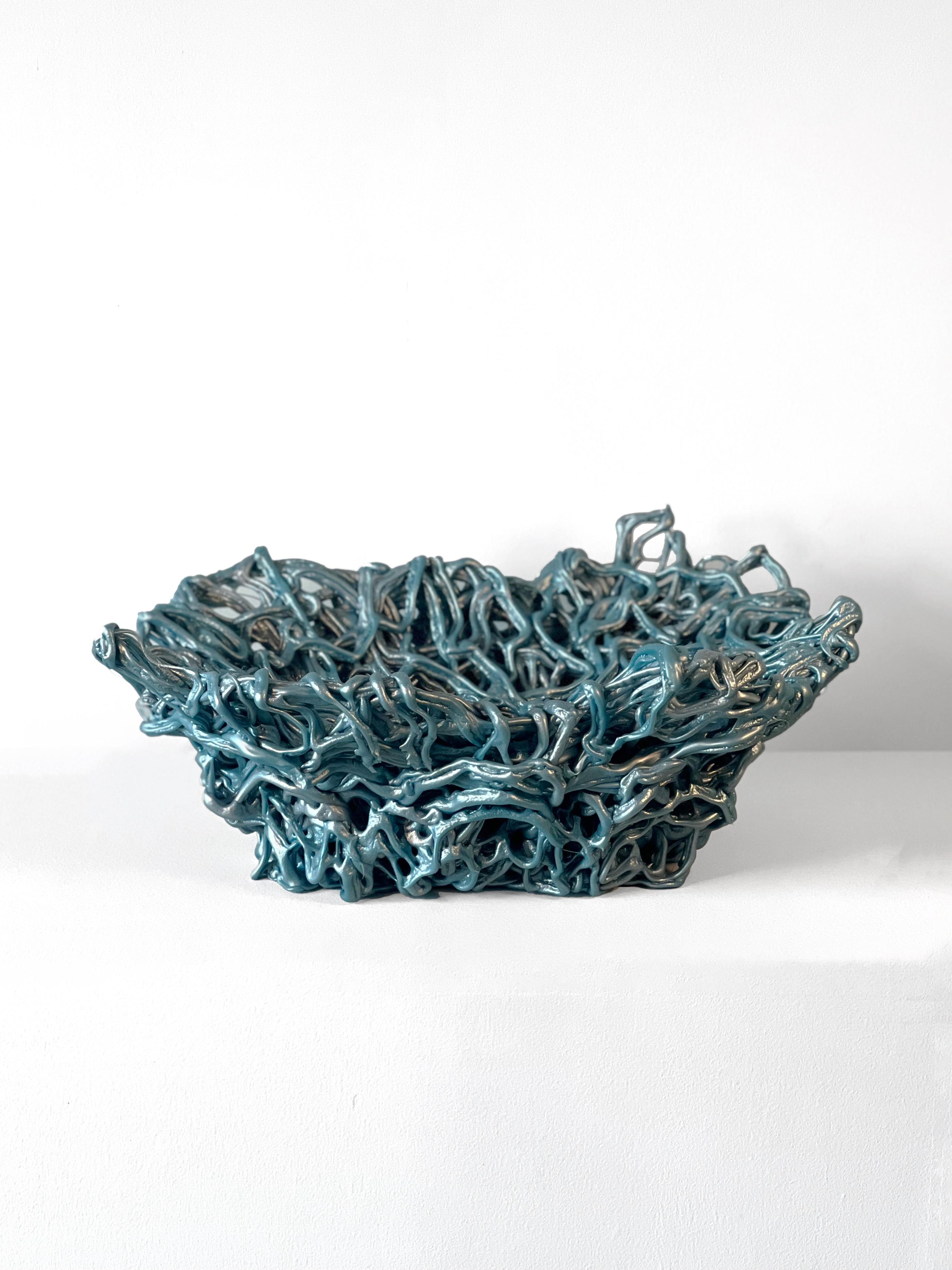 A unique and intricate piece that can take the form of a basket, vessel, or sculpture.  Teal and silver post-consumer plastic gets melted down and extruded to create this organic form vessel.  This piece explores the functionality of plastic beyond