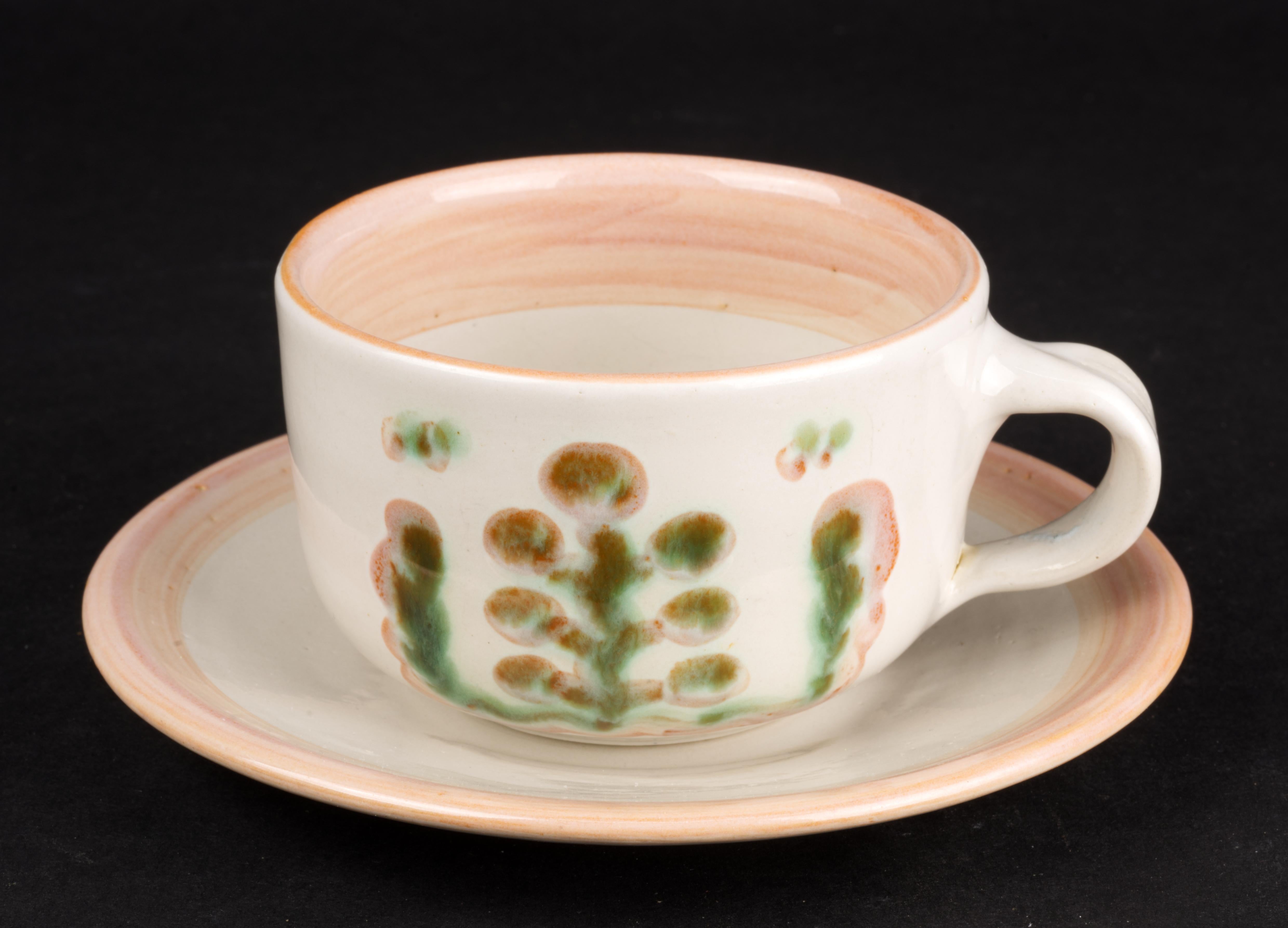  Tea or cappuccino cup and saucer were handmade by Hadley Pottery in Louisville, Kentucky. It is hand painted in minimal palette of green and pink with stylized plant and fruit designs done in thick glaze on off-white background and accented with