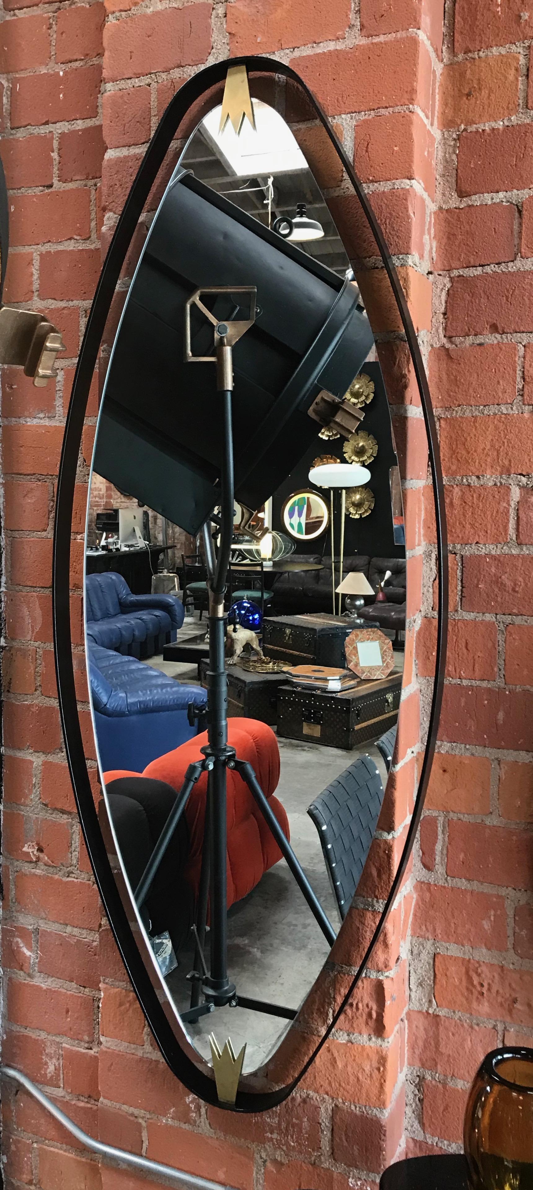 MA+39 oversized oval wall mirror in brass and black lacquered iron. The oval frame is obtained from a single curved iron plate with two elegant manufactured brass elements joining the mirror to the frame.