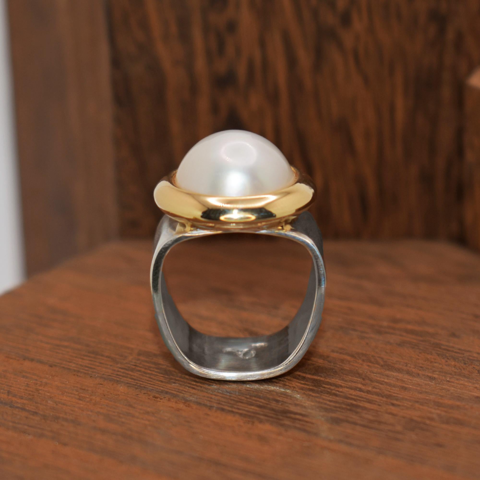 Freshwater Mabé Pearl set in a 14k yellow gold modern bezel on a wide sterling silver square shape ring band. Cocktail ring is size 7 and is resizable. Mabé Pearl measures 15mm across and 7mm in height. Ring band is 12mm in width. Contemporary,