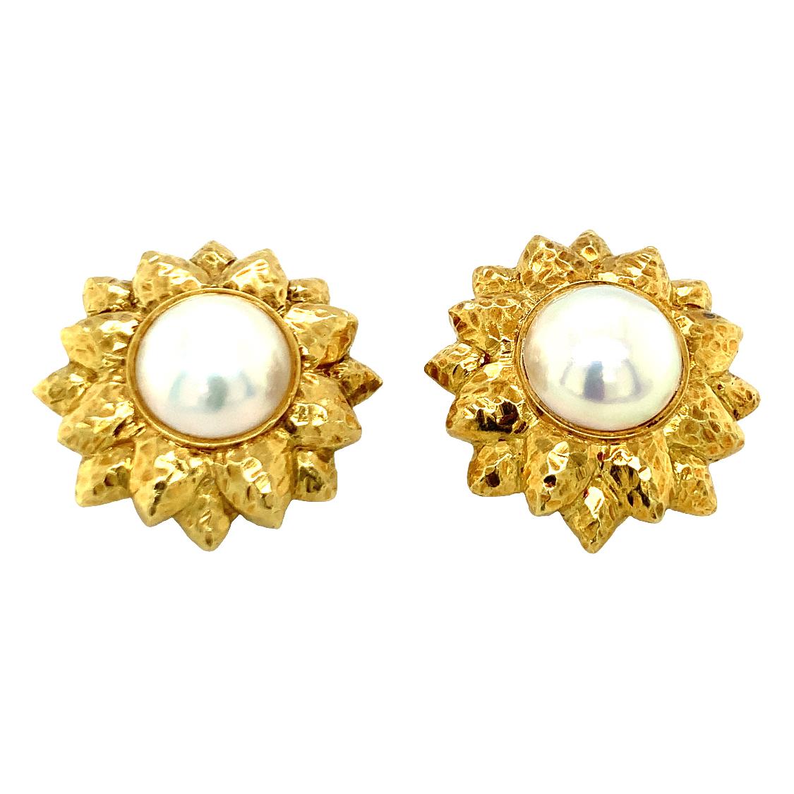 One pair of mabe pearl 18K yellow gold sunflower motif earclips featuring two bezel set, white mabe pearls each measuring 14 mm. in diameter. With a hammered gold finish throughout. Circa 1960s.

Showy, sheen, reflective.

Metal: 18K yellow