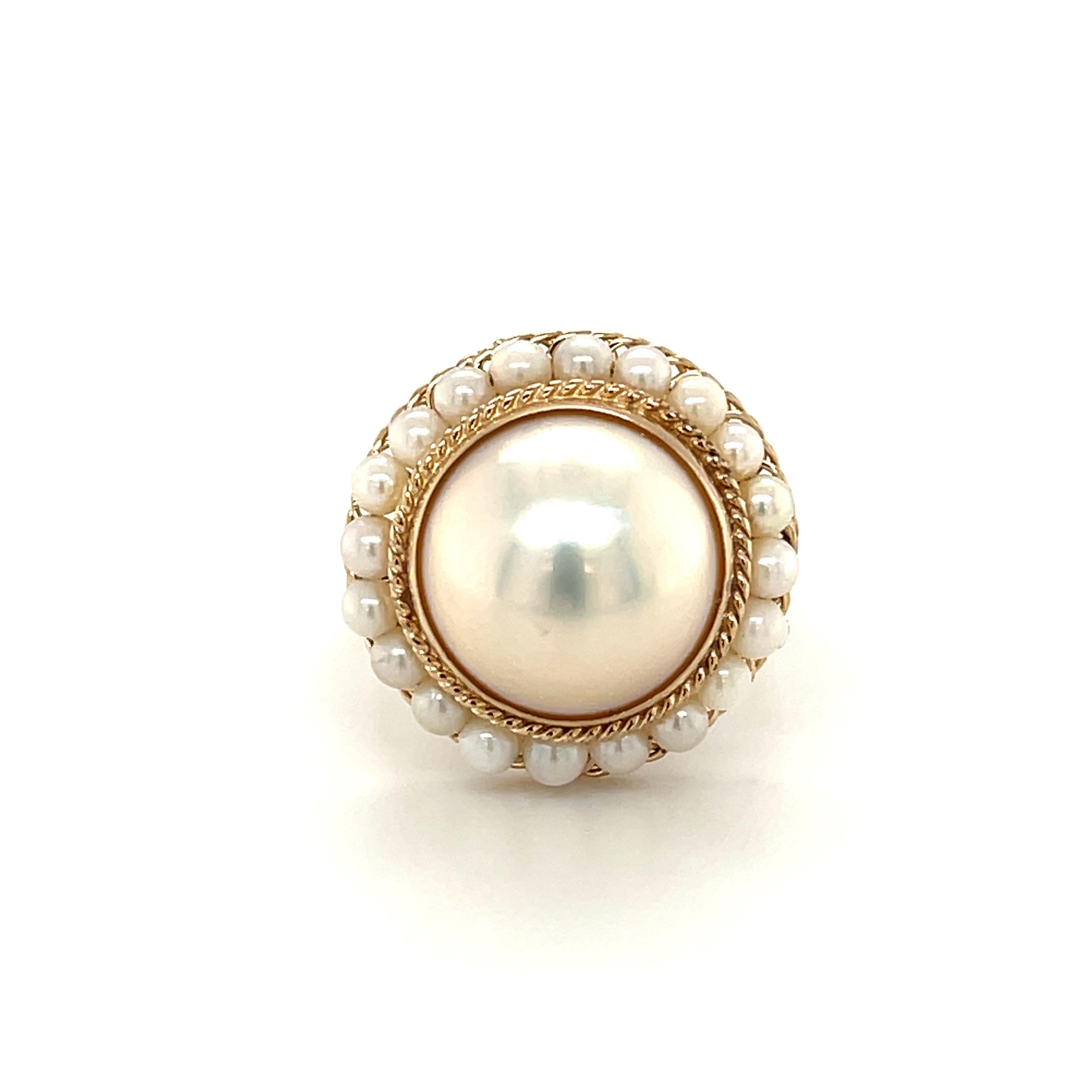 This timeless classic pearl ring features a gorgeous white Mabe pearl set in 14k yellow gold. The large center pearl measures 14mm, and is surrounded by delicate 3mm seed pearls. This ring showcases intricate hand made filigree gold work and fine