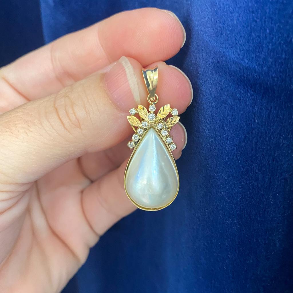 Questo ciondolo splendidamente conservato è pronto per essere amato di nuovo! Una deliziosa perla mabe a forma di pera si trova in un castone d'oro, accentuato nella parte superiore da diamanti e foglie d'oro strutturate che formano un dolce fiocco.