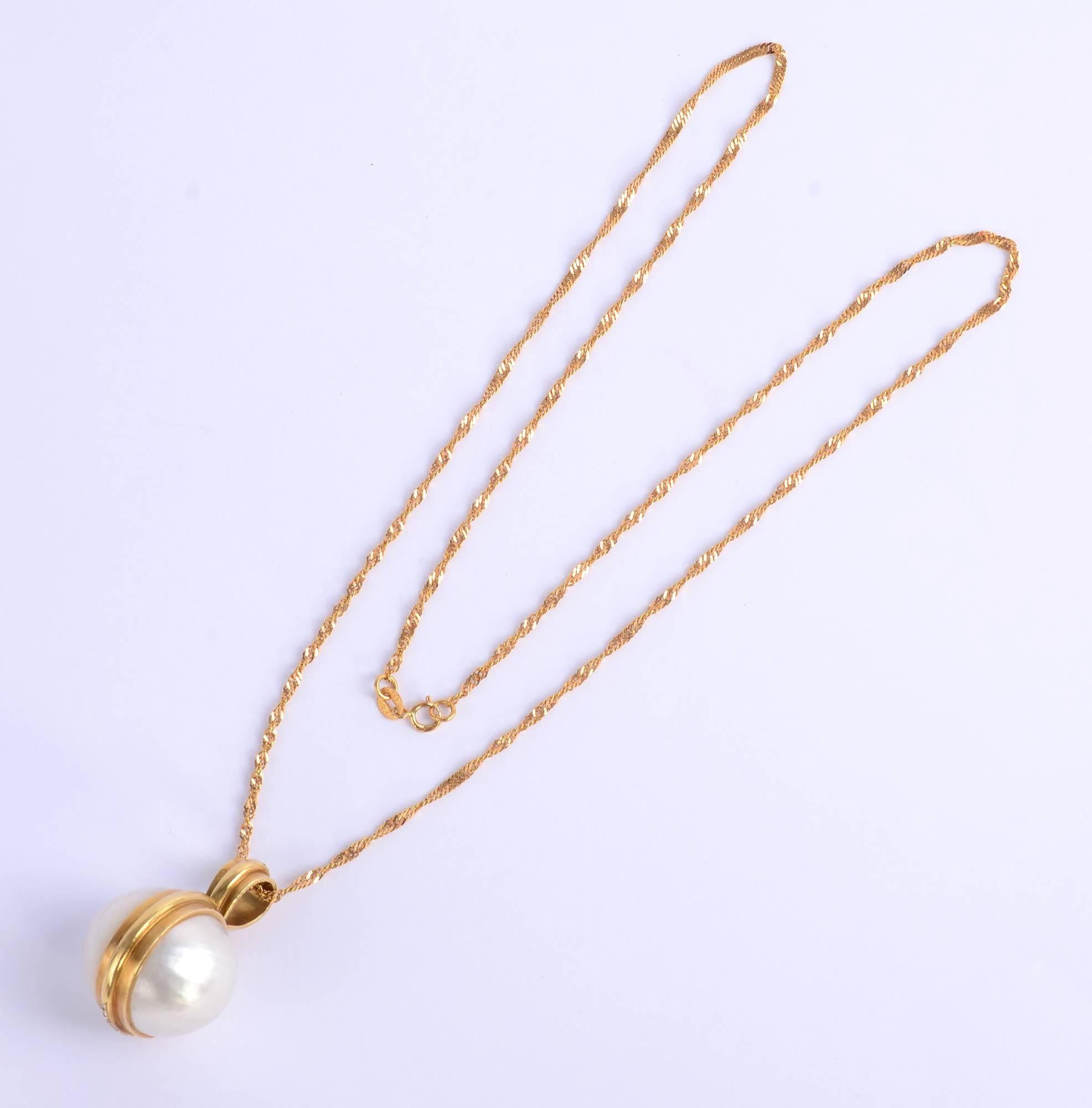 A huge mabe pearl (approximately 25 mm in diameter) is banded with gold in this unusual pendant necklace. One side of the double layer banding, including the hanging loop, is filled with diamonds. The pendant measures 
1  1/2 inches to the top of