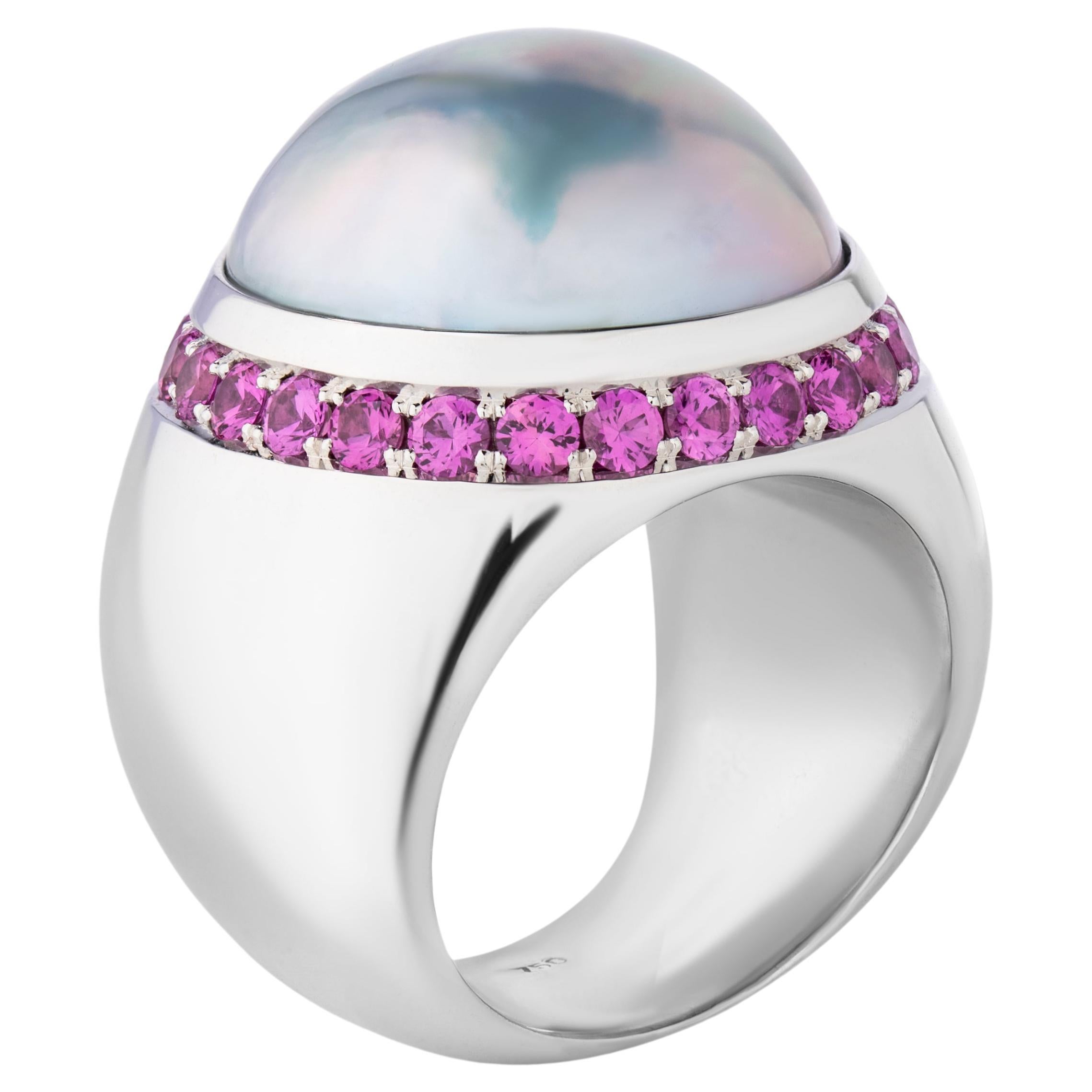 Lujoso anillo de oro blanco de 18 quilates, una gran perla mabé de 19,40 mm rodeada de 26 zafiros rosas con un total de 1,92 quilates.
La enorme perla mabé de muy buen brillo y su bella iridiscencia como pieza central está acentuada por 26 zafiros