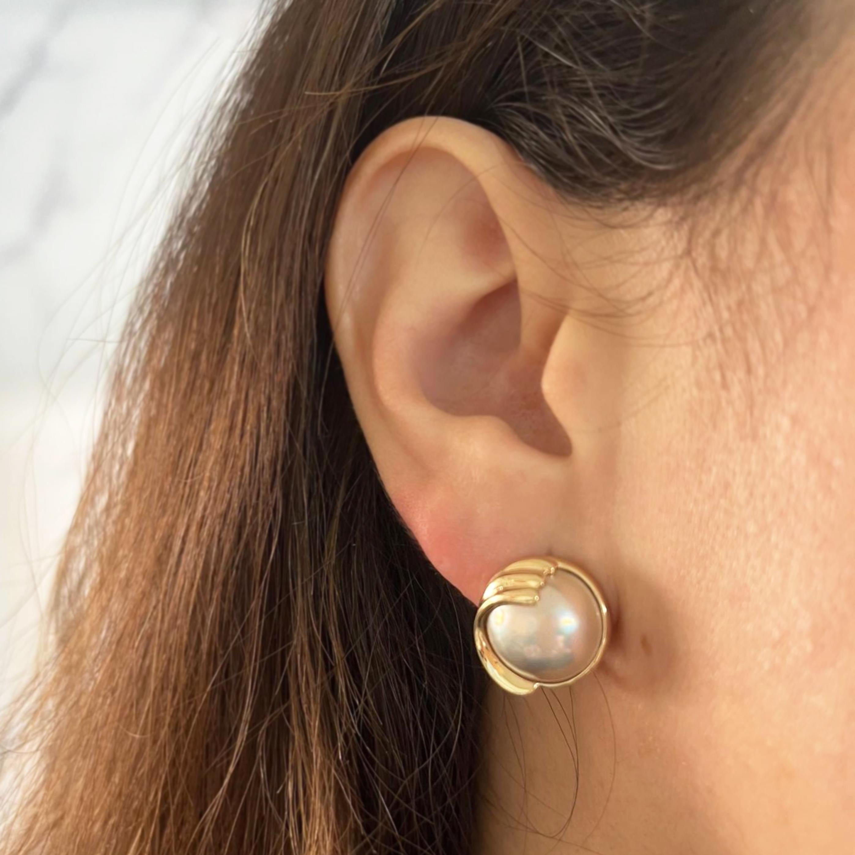 14 karat yellow gold stud earrings featuring 13mm round mabe pearls accented by a wave border. Pierced post with omega clip back. Post Removed Upon Request. Finished weight is 8.4 grams.
