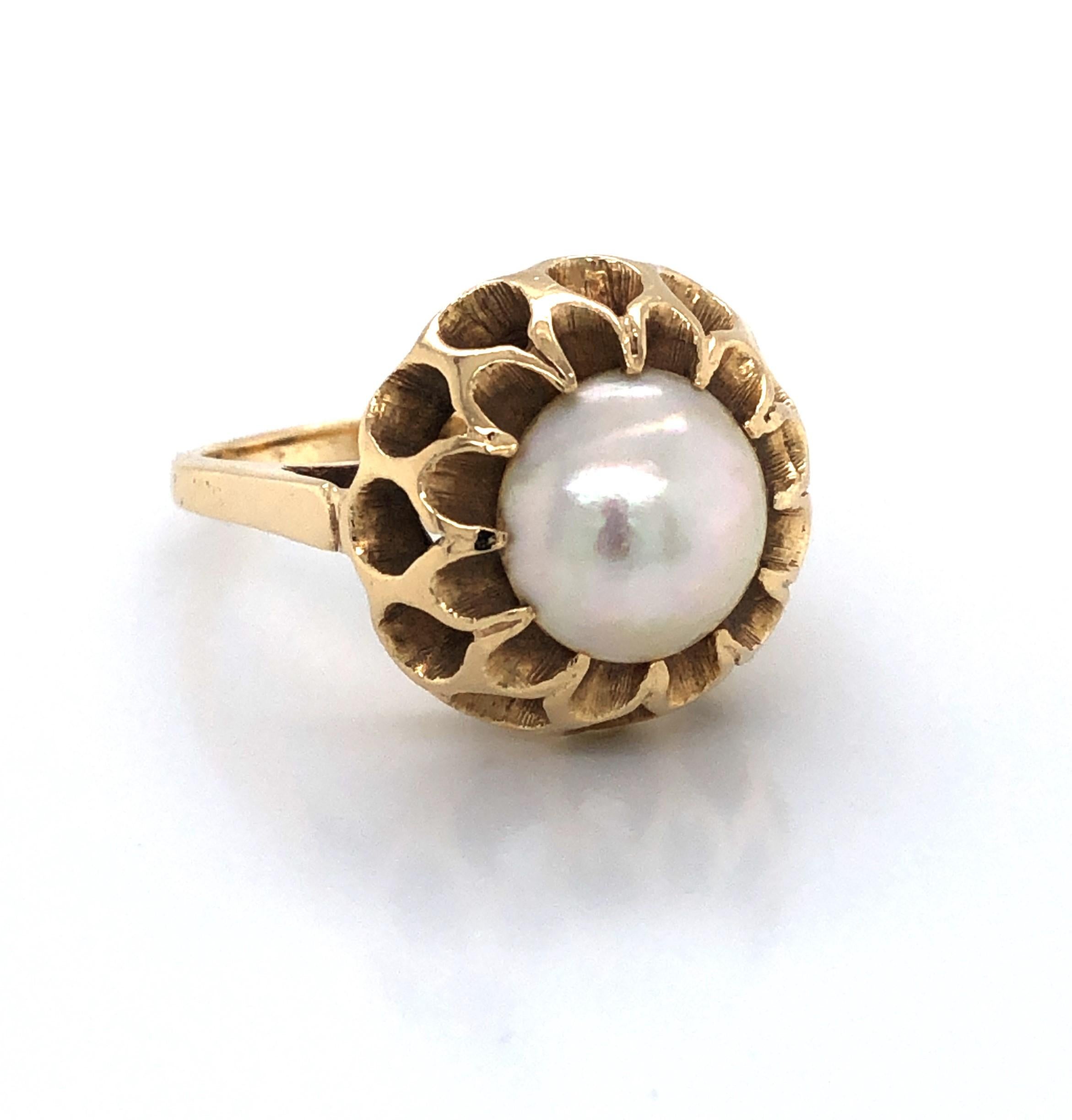 A lacy pattern of bright and satin textures in fourteen karat 14K gold intricately form this floral inspired dome ring. Crowning the bud is a large 10.5 mm iridescent Mabe pearl. The ring head measures approximately 3/4 inch wide, with a 1/4 inch