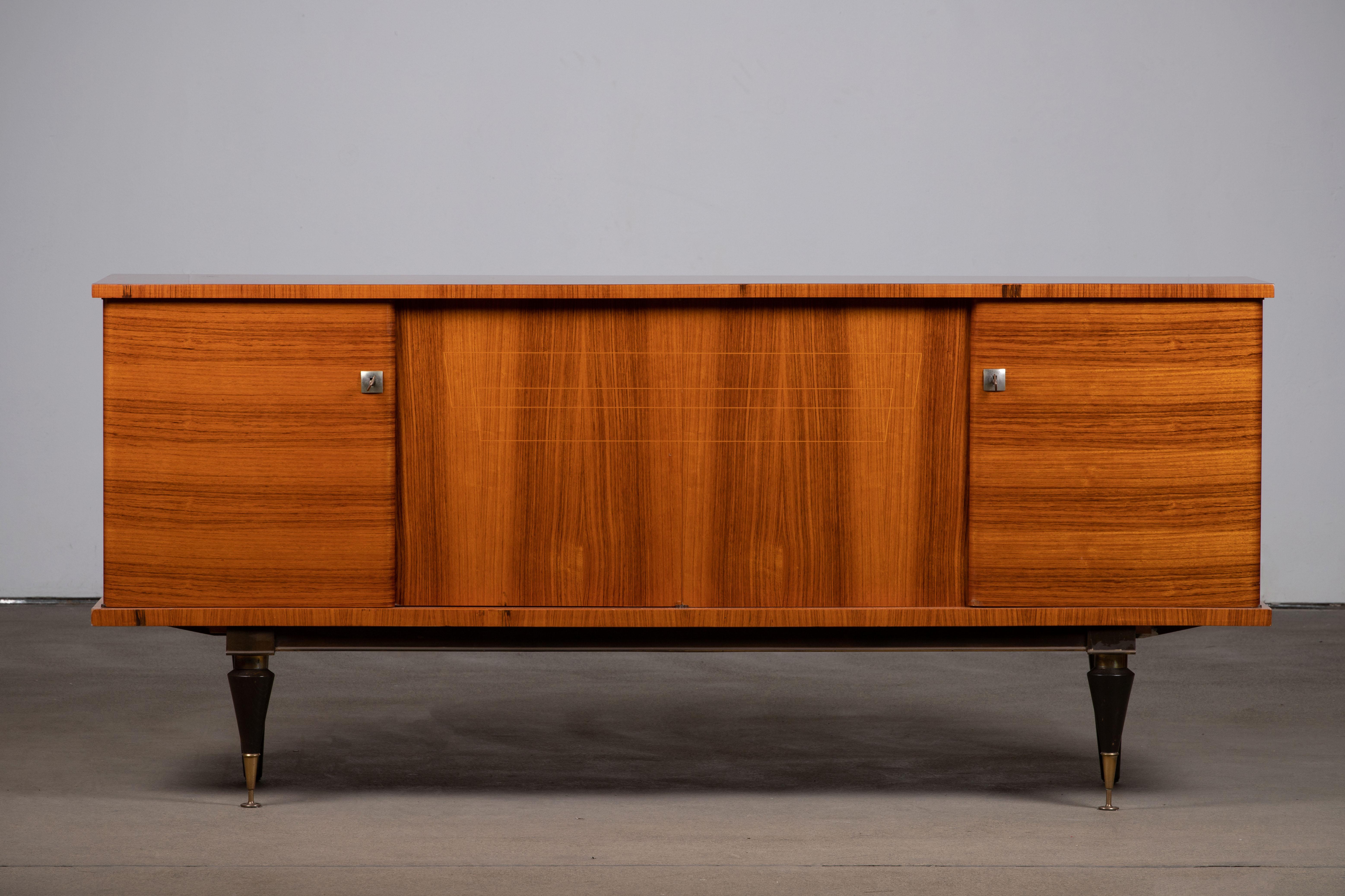 French Art Deco sideboard, credenza, with bar cabinet. The sideboard features stunning Macassar wood grain and rich pattern. It offers ample storage, with shelves and a column of drawers. The case rests on tall tapered legs with brass details. A