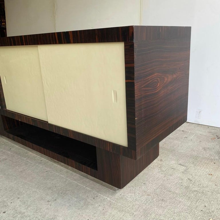 Art Deco sideboard with fine finish of Macassar ebony and milk glass or off-white glass sliding doors. Plinth base includes additional storage and chrome trim at floor. Large chrome pull at door is original and fantastic. France or Austria, 1930's.