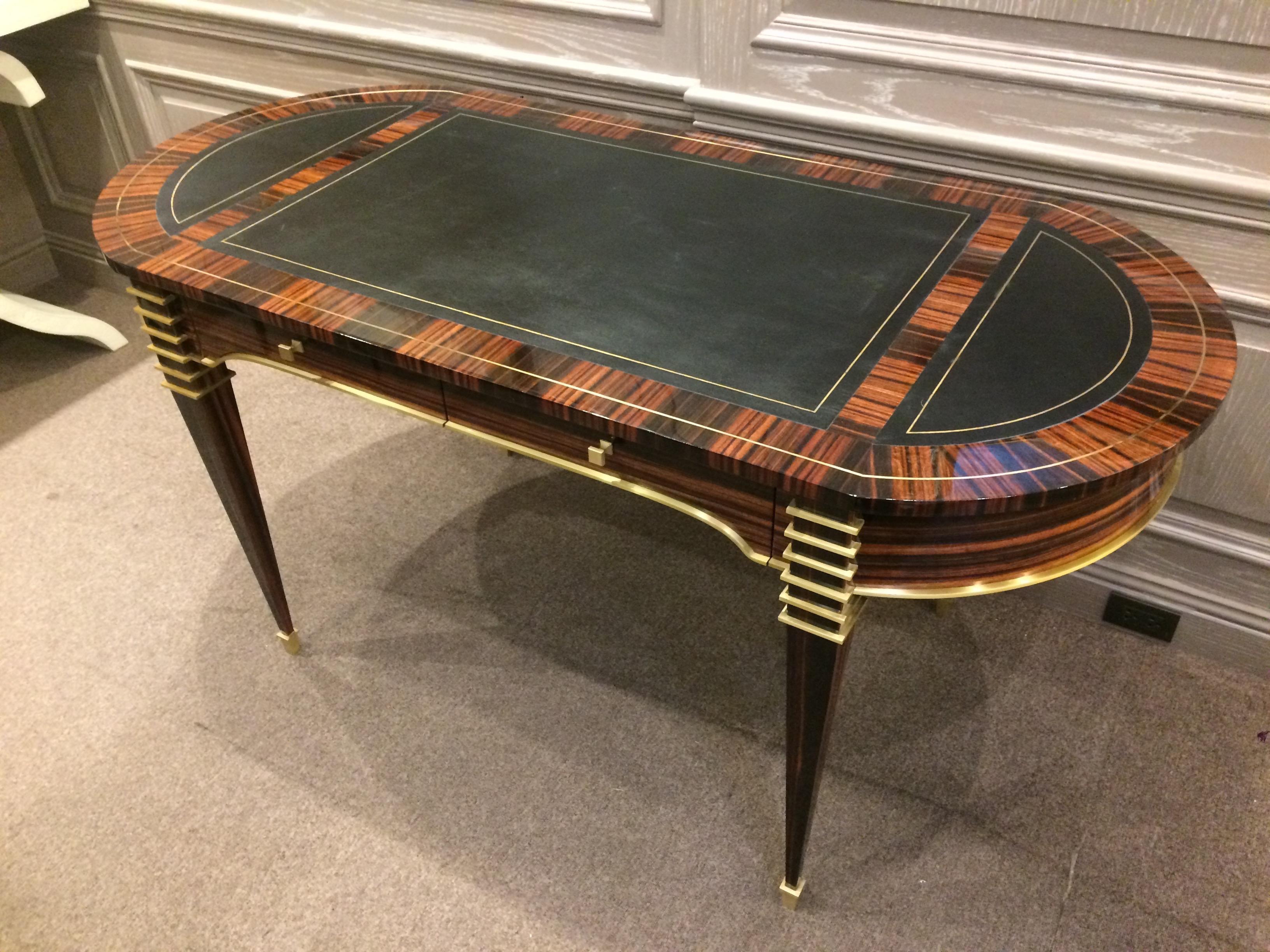 The Helene desk, the oval shaped top is cross-banded with natural Macassar ebony and inlaid with brass stringing. The top is divided into three black leather and gold leaf hand tooled writing surfaces. The apron contains two drawers on the front