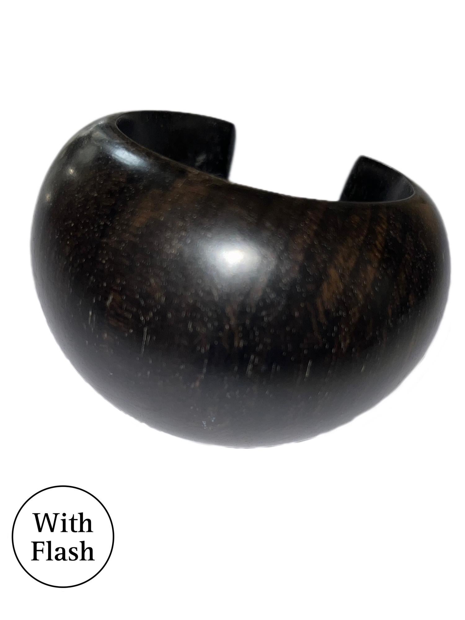 Ce bracelet est un grand bracelet simple mais saisissant. Le bracelet est en ébène de Macassar, un bois exotique et rare de couleur foncée. Le style du bracelet rappelle les créations de la joaillière française Catherine Noll. 

Les mesures sont