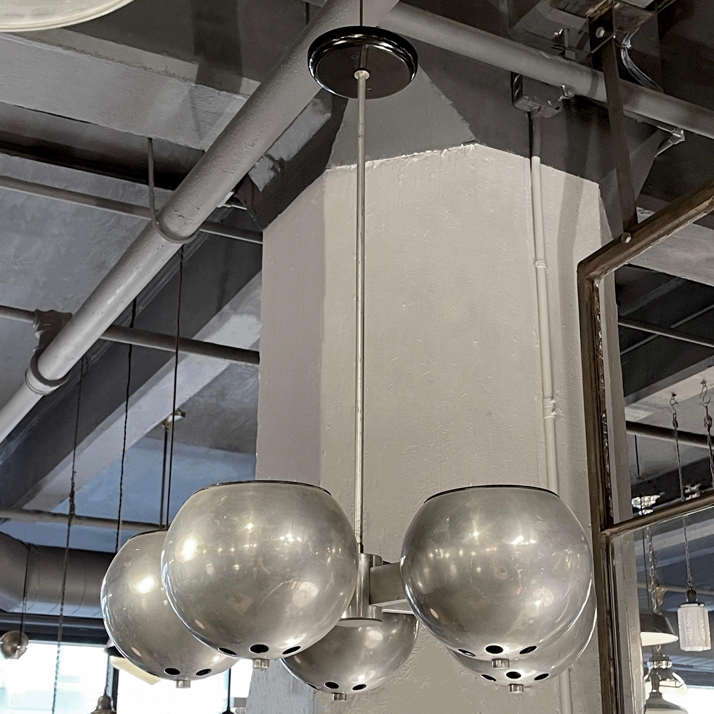 Mid-century, machine-age, art deco style chandelier features five arms with perforated open globes that cast light up and down through the perforations on a fixed pole with contrasting black canopy.
 