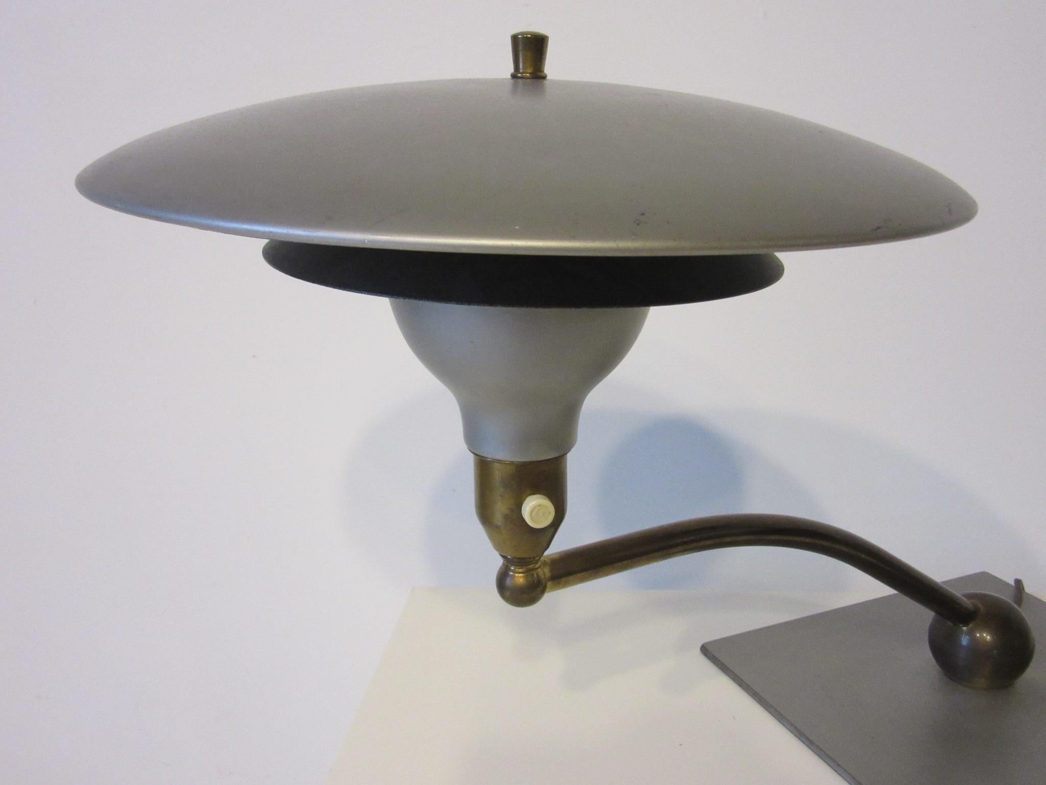 A machine aged desk lamp with painted metal shades and brass swing arm mounted on a brass ball and plate. Retains the original labels the sight light lamp and was manufactured by the M.G. Wheeler Company.