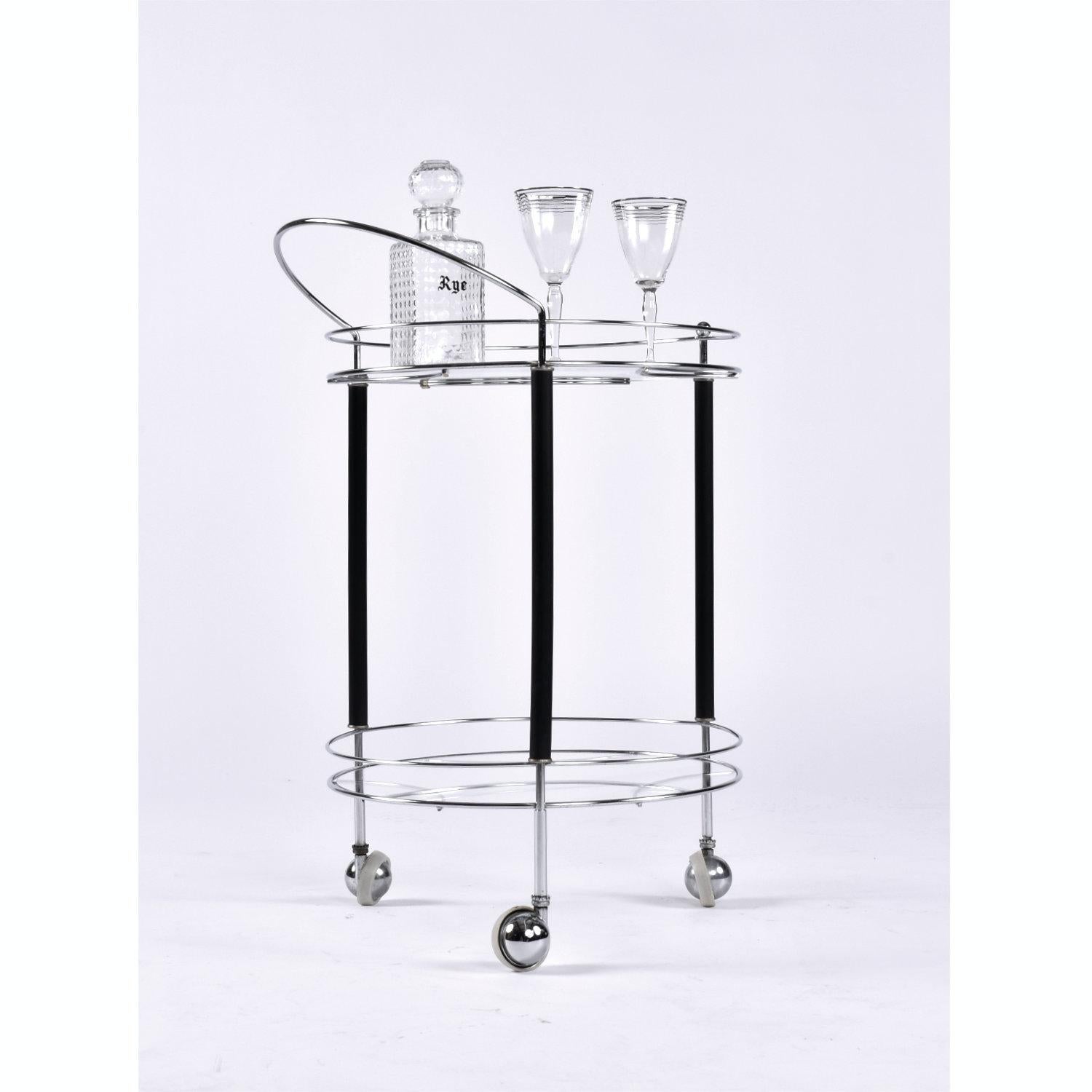 Sleek chrome, black and glass round bar cart on wheels. This piece captures elements of Art Deco, Machine Age and mid-century modern design. Dating from the early 1950s, one can see the layover from earlier aesthetic movements. The chrome finish