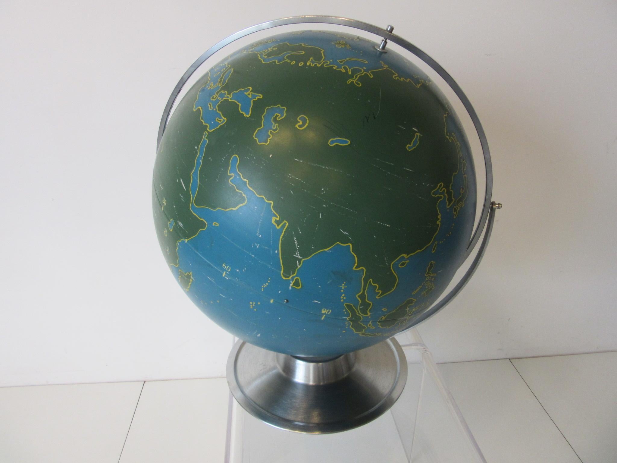 A metal rotating globe with painted countries, bodies of water, latitude and longitude numbers used for aviation and military navigational training with brushed stainless steel base and ring. This large very well crafted hollow globe is the tops for