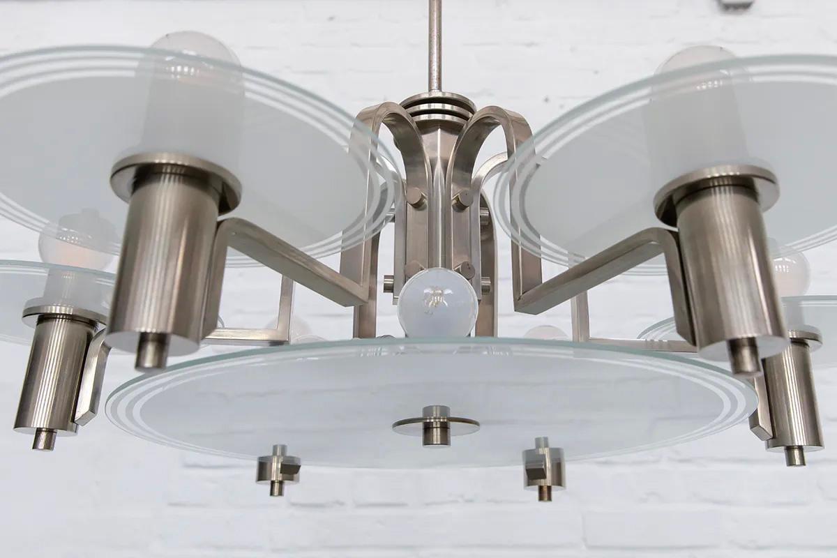 Esta sorprendente lámpara de araña alemana, fabricada hacia 1930, es un ejemplo raro y excepcionalmente bien conservado del modernismo expresionista y del diseño de alta gama de la Edad de las Máquinas. La composición está dominada por elementos de