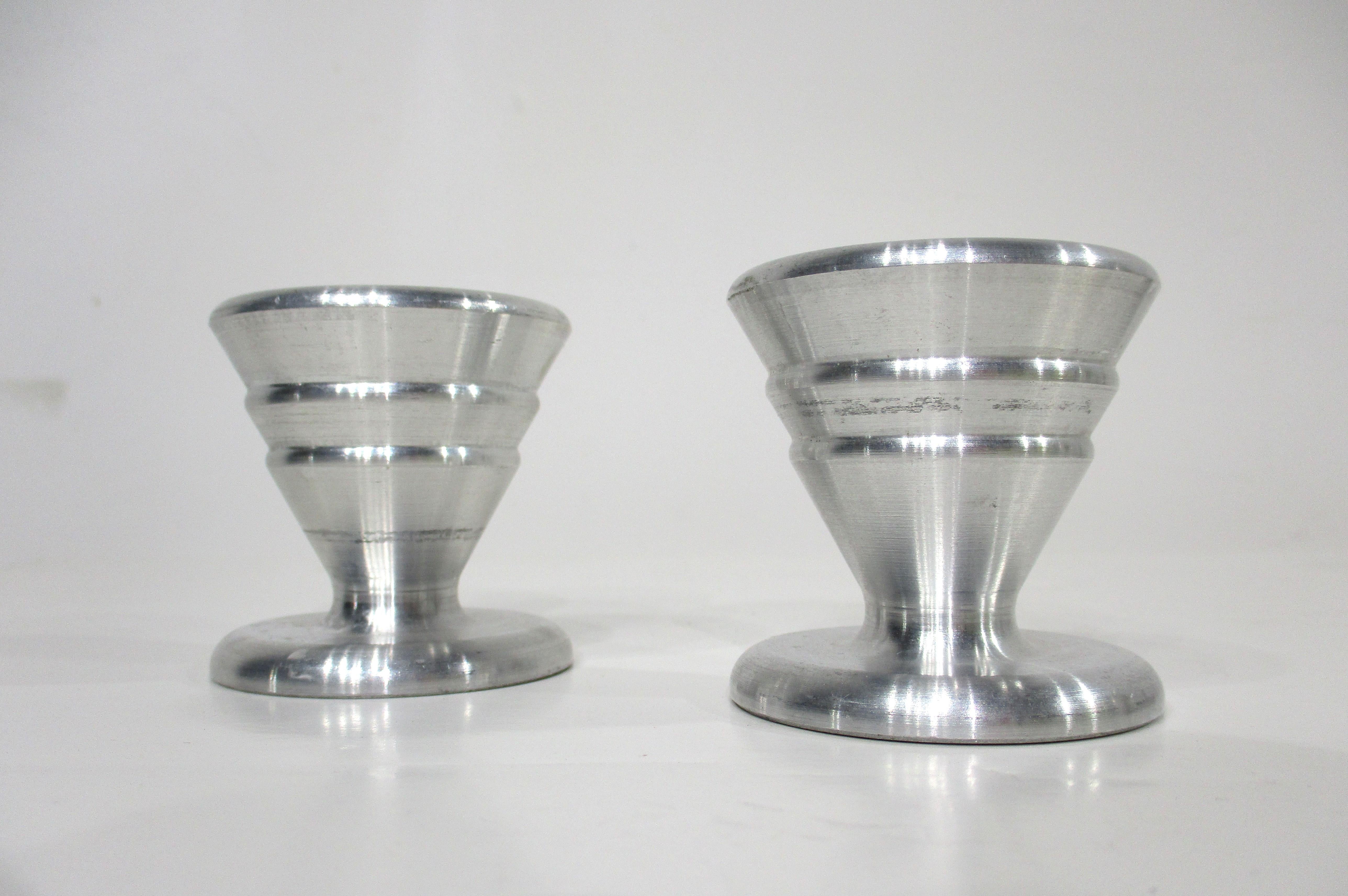 A pair of machine age turned solid aluminum candlesticks with tapered bodies and graduated design details . A great pair that would work with a mid century , art deco or simple streamline interior .  