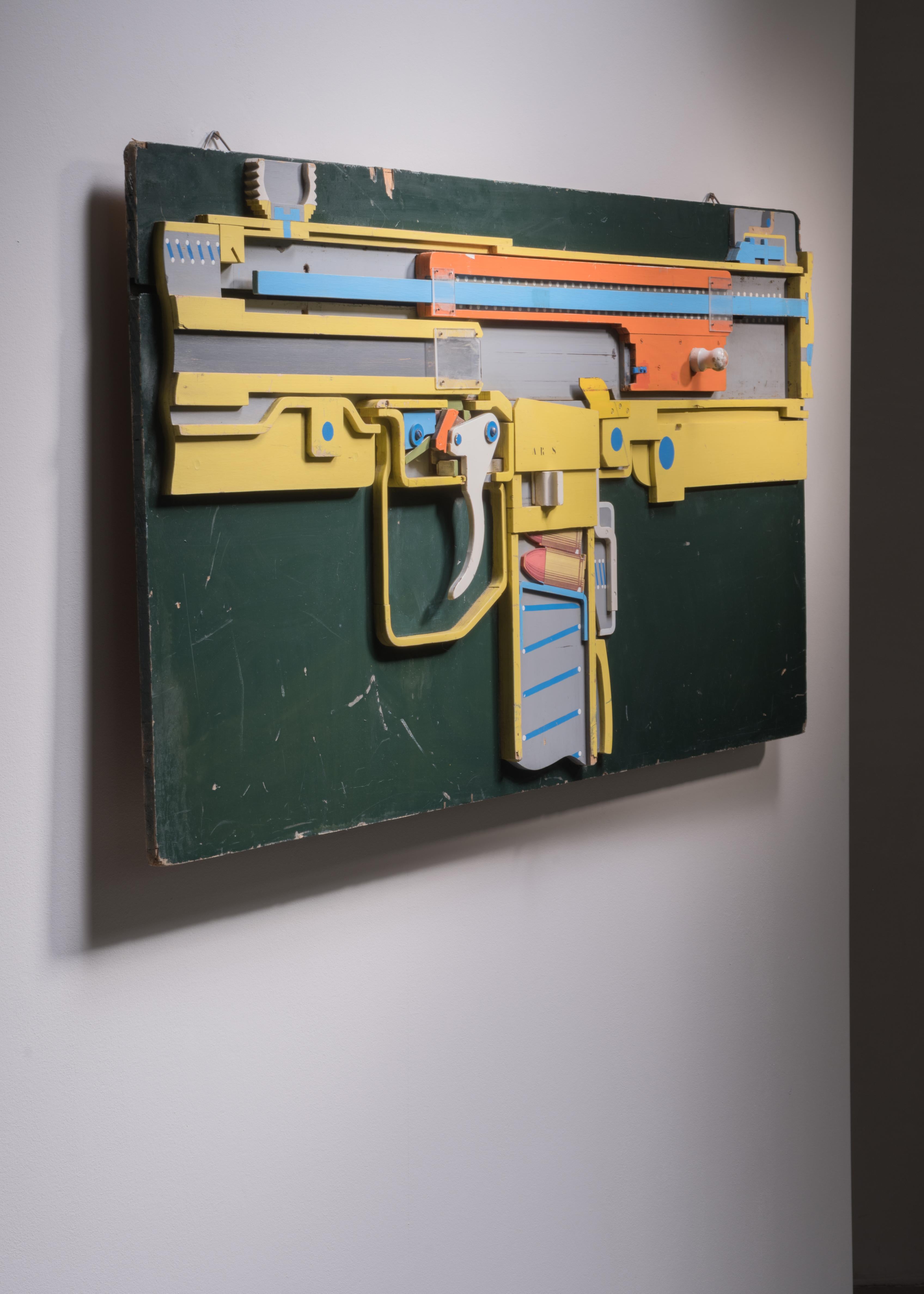 A decorative section model of part of a machine gun, made of painted wood on a wooden panel. We have three variations of these models available. They were made for educational purposes, the mecinics work in 2D and the simplification, craftmanship of