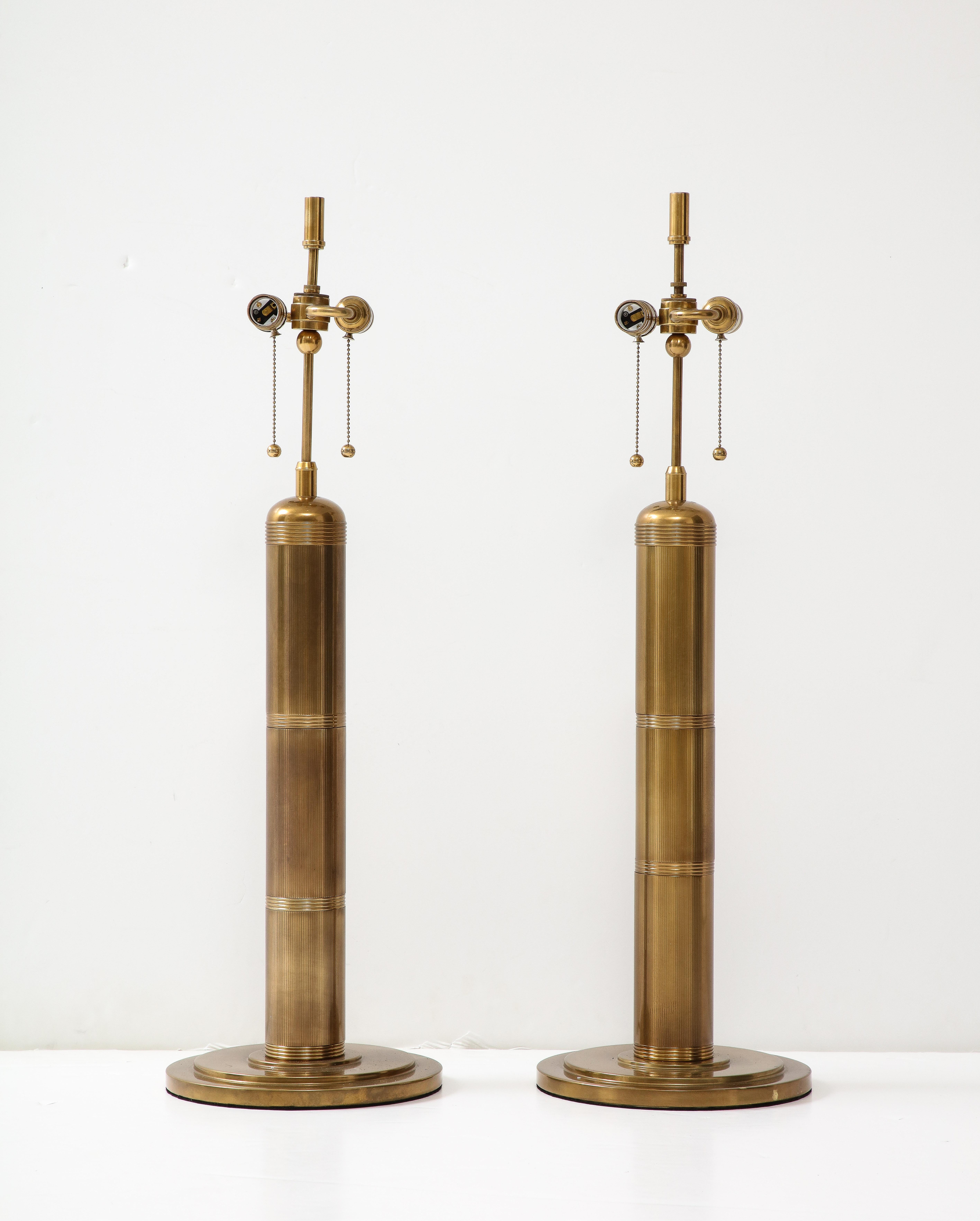 Modernist pair of bronze lamps with machine engraved column bodies and stepped disc bases. Lamps feature double pull chain sockets. Rewired for use in the USA with brown fabric cords by an UL listed electrician. 75W bulb max each bulb, unless LED.
