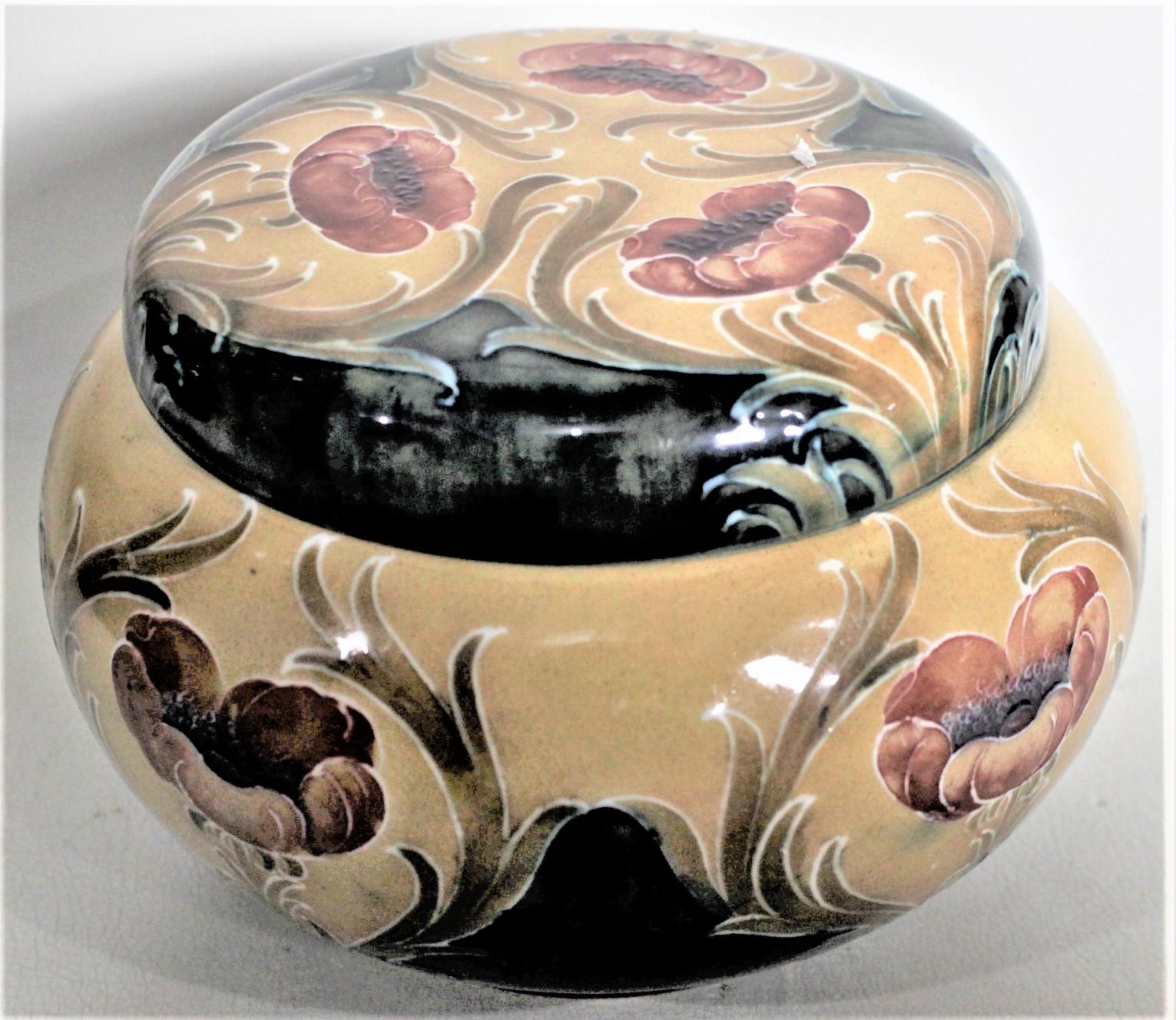 This antique art pottery covered tobacco or dresser jar was made by the James MacIntyre company of England, under the design direction of William Moorcroft, in circa 1890 in the period Victorian style. The jar is done in a deep mustard ground with