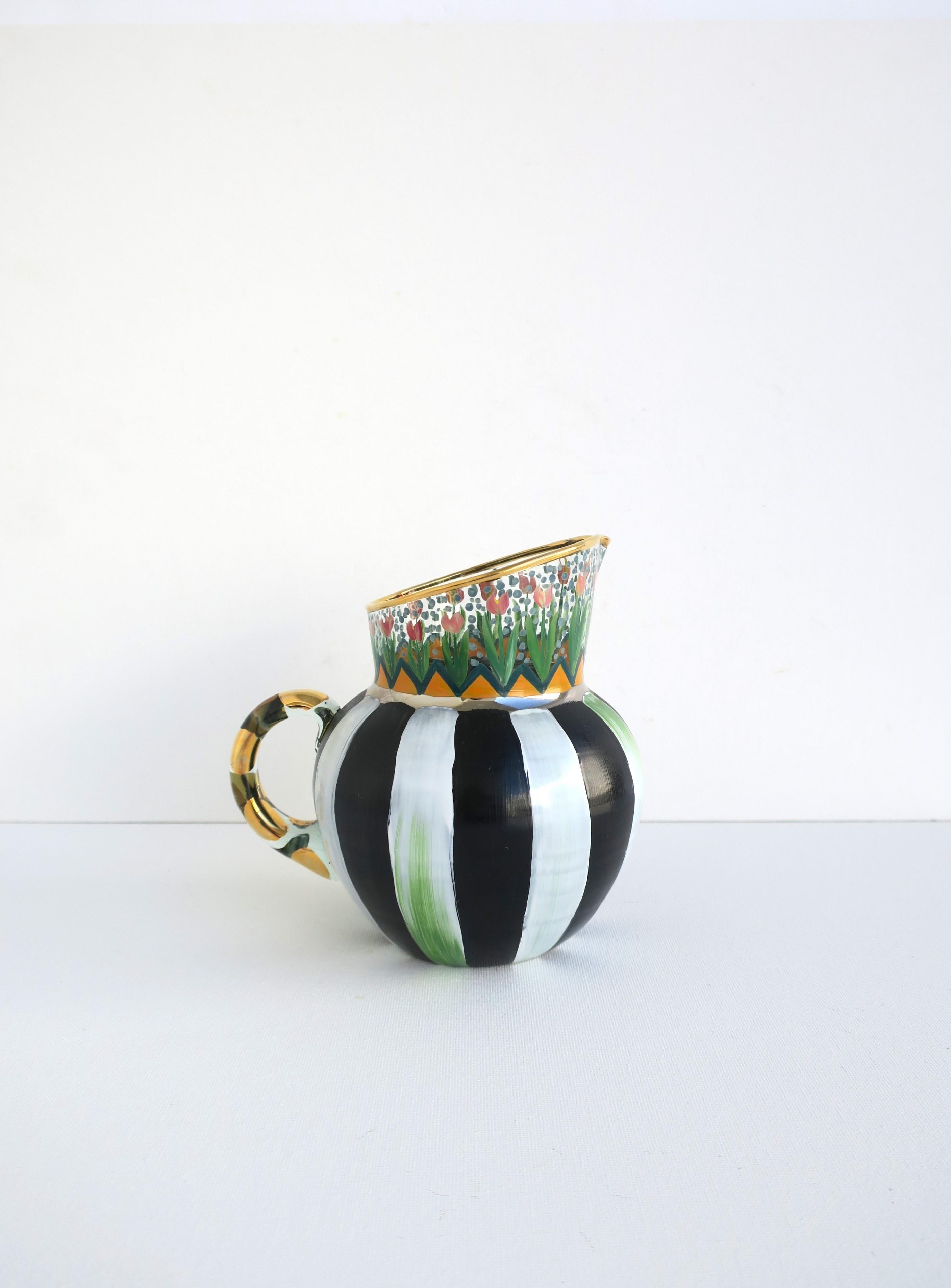 A beautiful authentic designer hand-painted art glass pitcher by designers' MacKenzie-Childs, circa 1990s, New York. Pitcher has a hand-painted red tulip flower garden motif and an orange fence-like design around, finished with a gold rim, base is