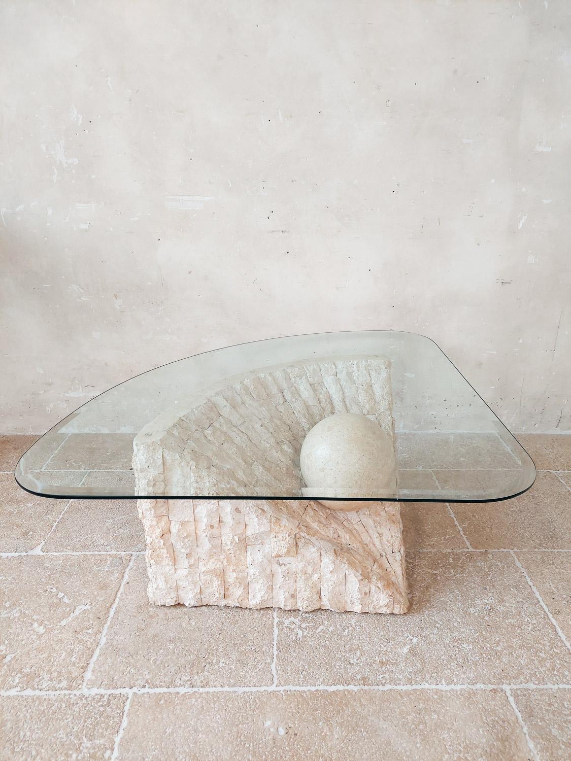 Mactan stone coffee table by Magnussen Ponte, 1980s. Unique postmodern design with a textured and geometric base with a suspended sphere which holds the triangular glass top. 

Mactan is a natural stone, although this piece looks heavy and