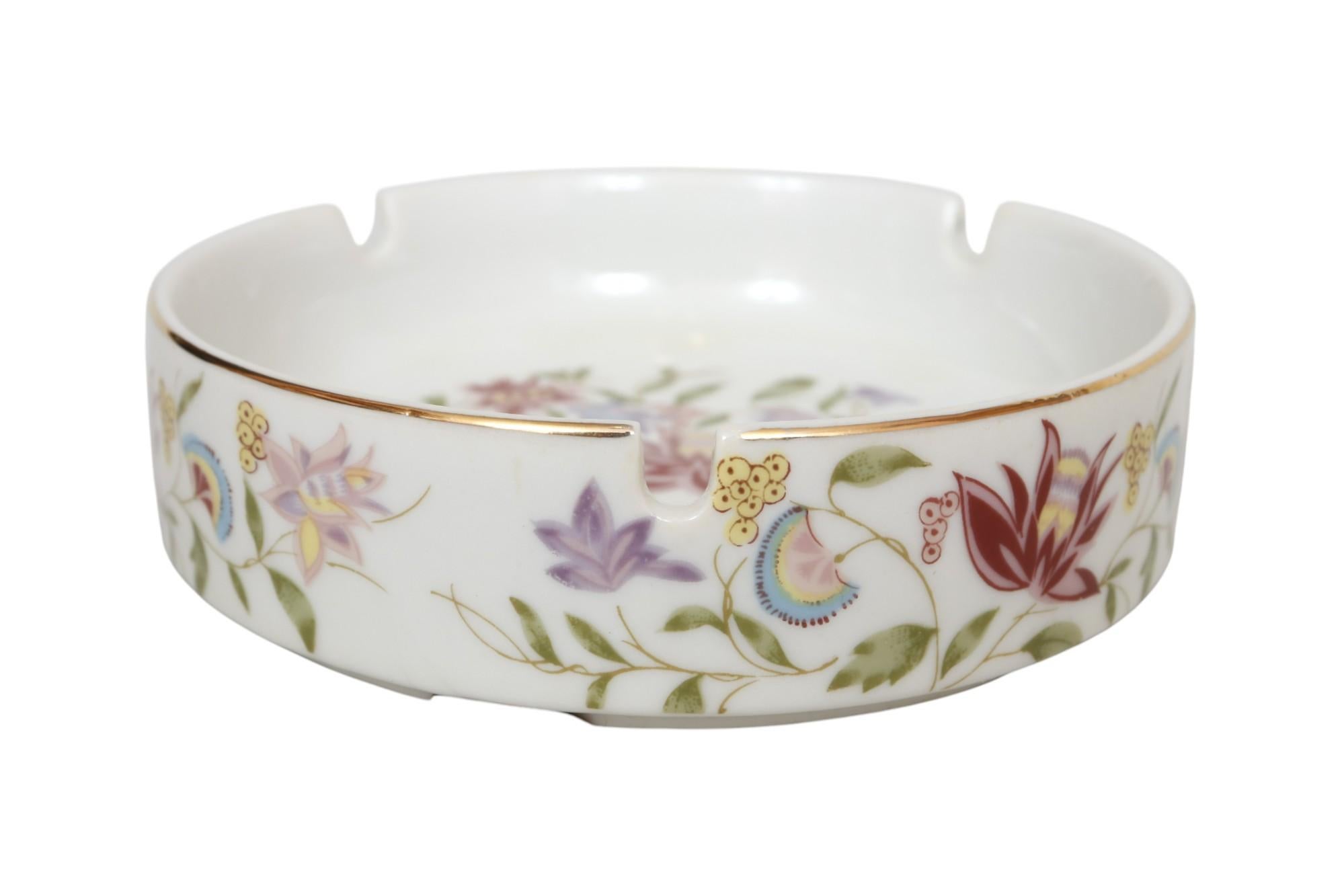 Cendrier floral rond en céramique fabriqué au Japon pour Macy's, vers 1990. Le cendrier blanc comporte trois repose-cigarettes et est décoré d'un motif floral rose, violet et jaune, et garni d'un bord doré. Marqué en dessous 