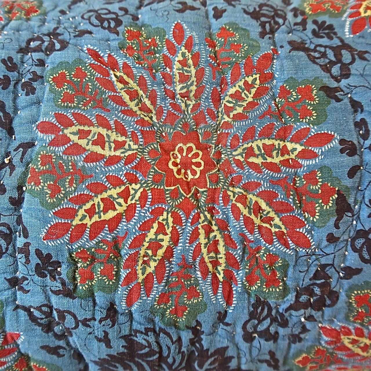 French, circa 1820s cotton block printed and quilted cushion in a striking design of bright saffron yellow and madder stylized flower heads surrounded by dark leaves on a blue pastel ground. With antique French natural indigo dyed tassels at each