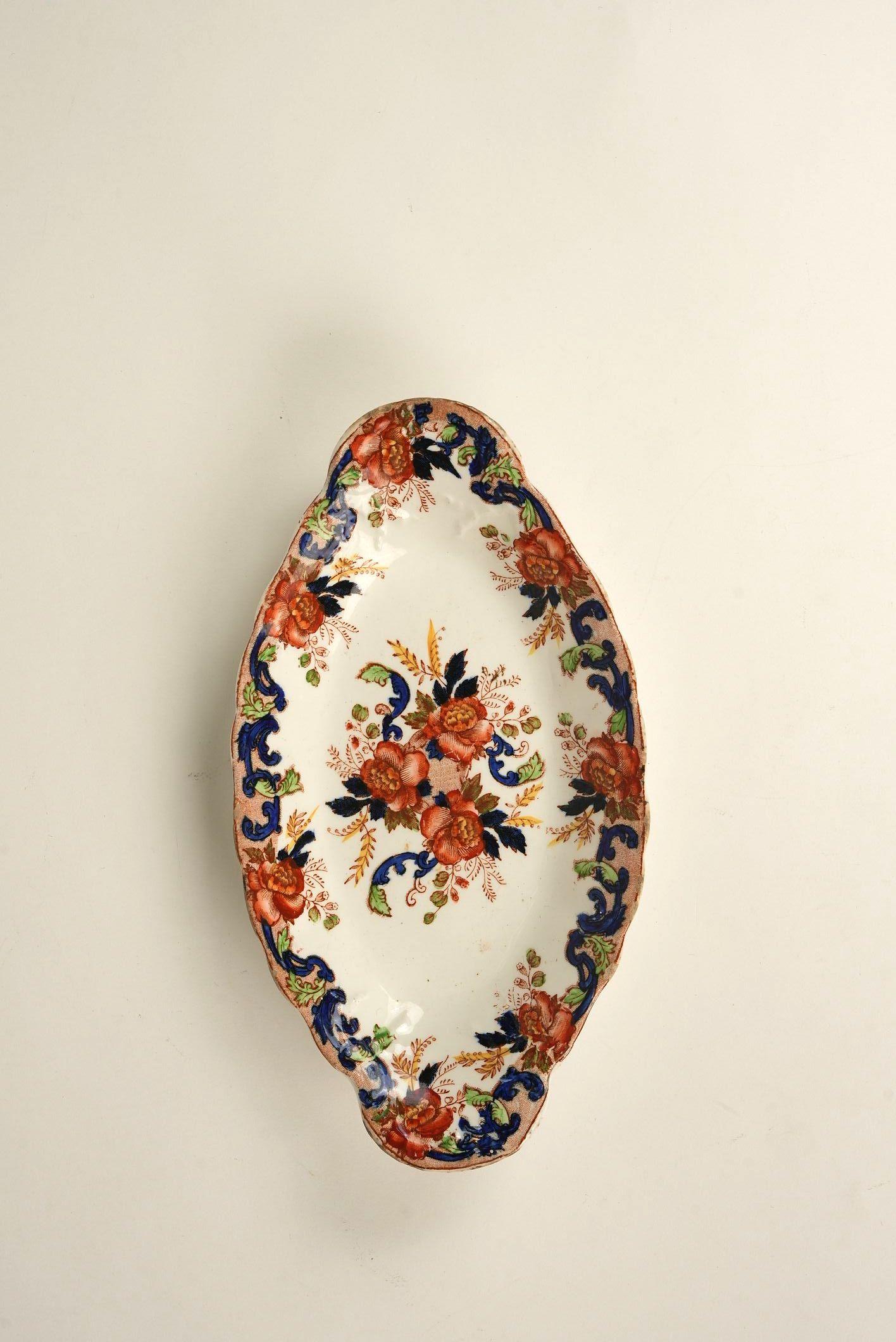 Este encantador plato ovalado de Maddock & Sons presenta una alegre explosión de flores enmarcada en una espectacular paleta de colores carmesí, azul marino y esmeralda. Su marcado aire barroco y su estampado floral simétrico la convierten en un